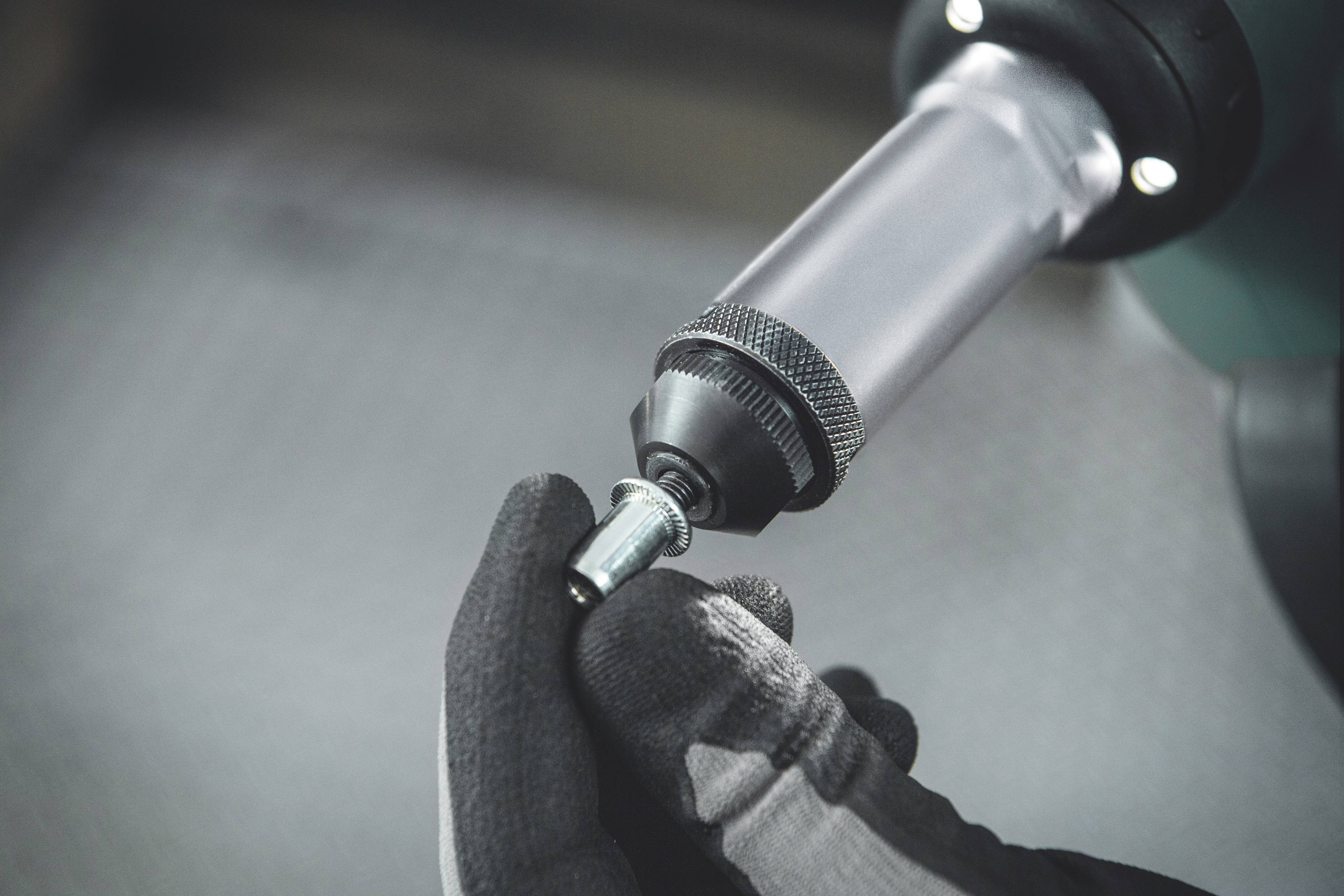 Eine mit Handschuhen bekleidete Hand hält eine kleine Metallkomponente an einen elektrischen Schraubenschlüssel, der gerade benutzt wird.