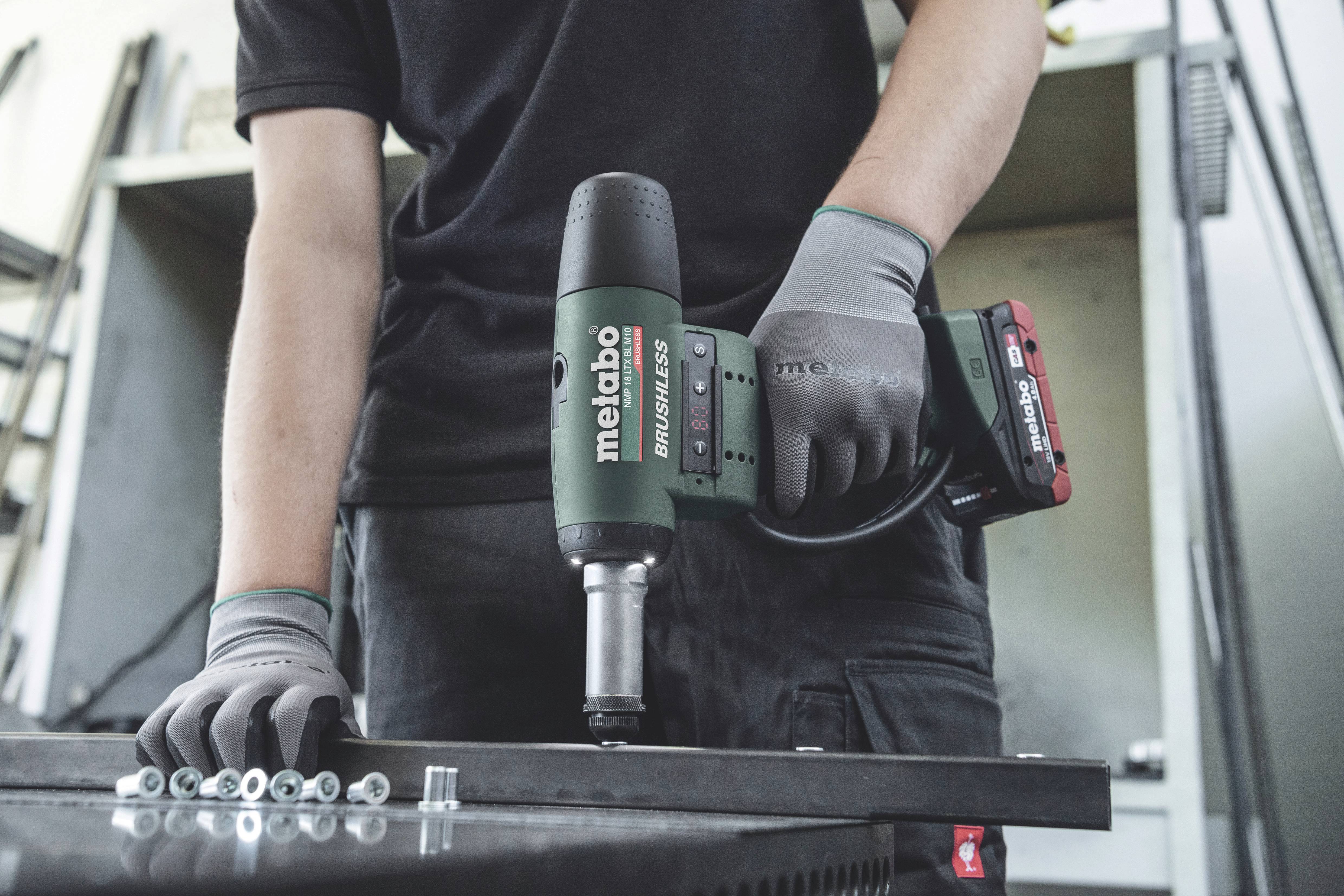 Person hält einen Metabo Akkuschrauber und arbeitet an einem Metalltisch. Schrauben liegen auf der Arbeitsfläche.