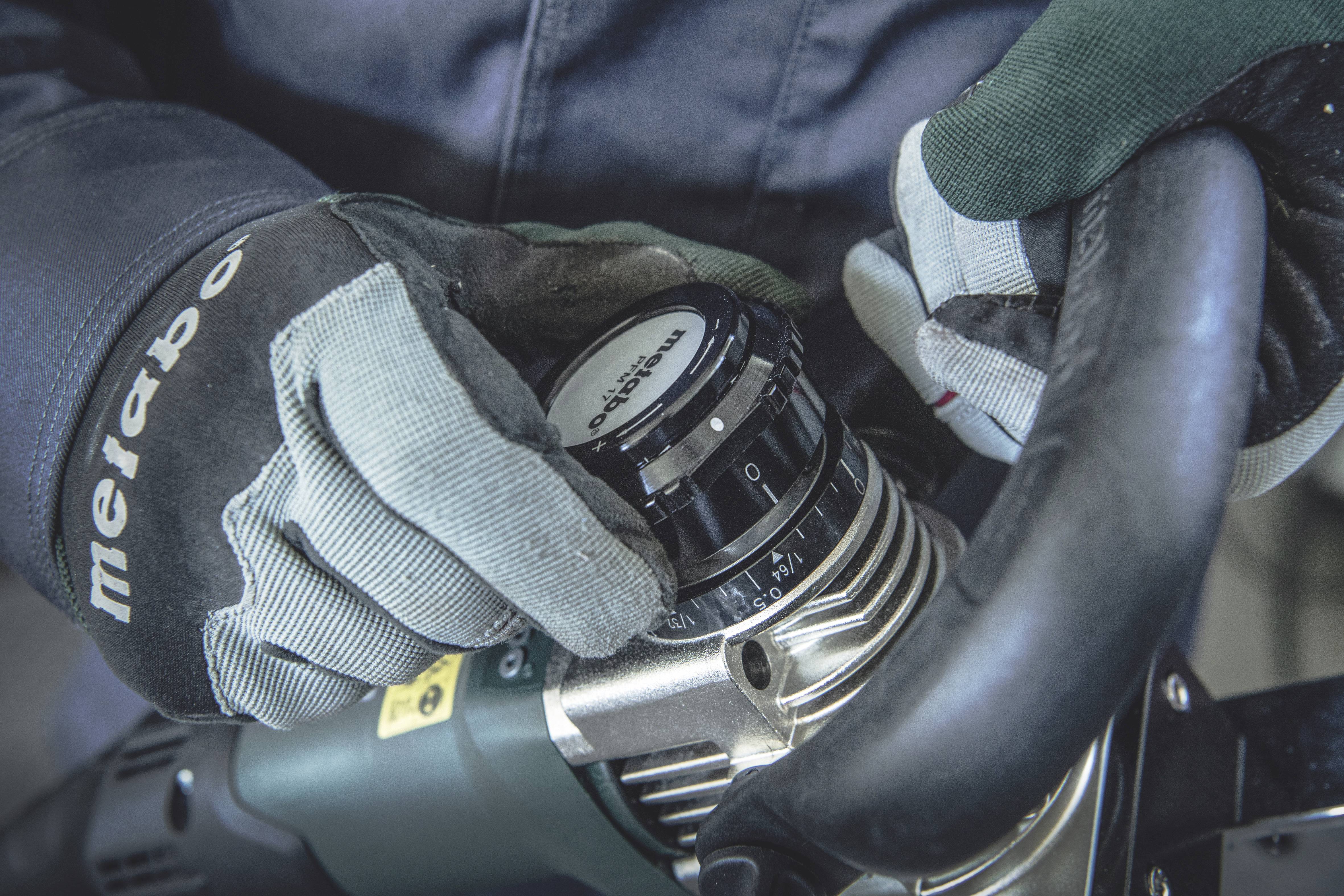 Eine Person mit Handschuhen stellt einen Drehknopf an einem elektrischen Werkzeug ein. Der Fokus liegt auf den Händen und dem Knopf.