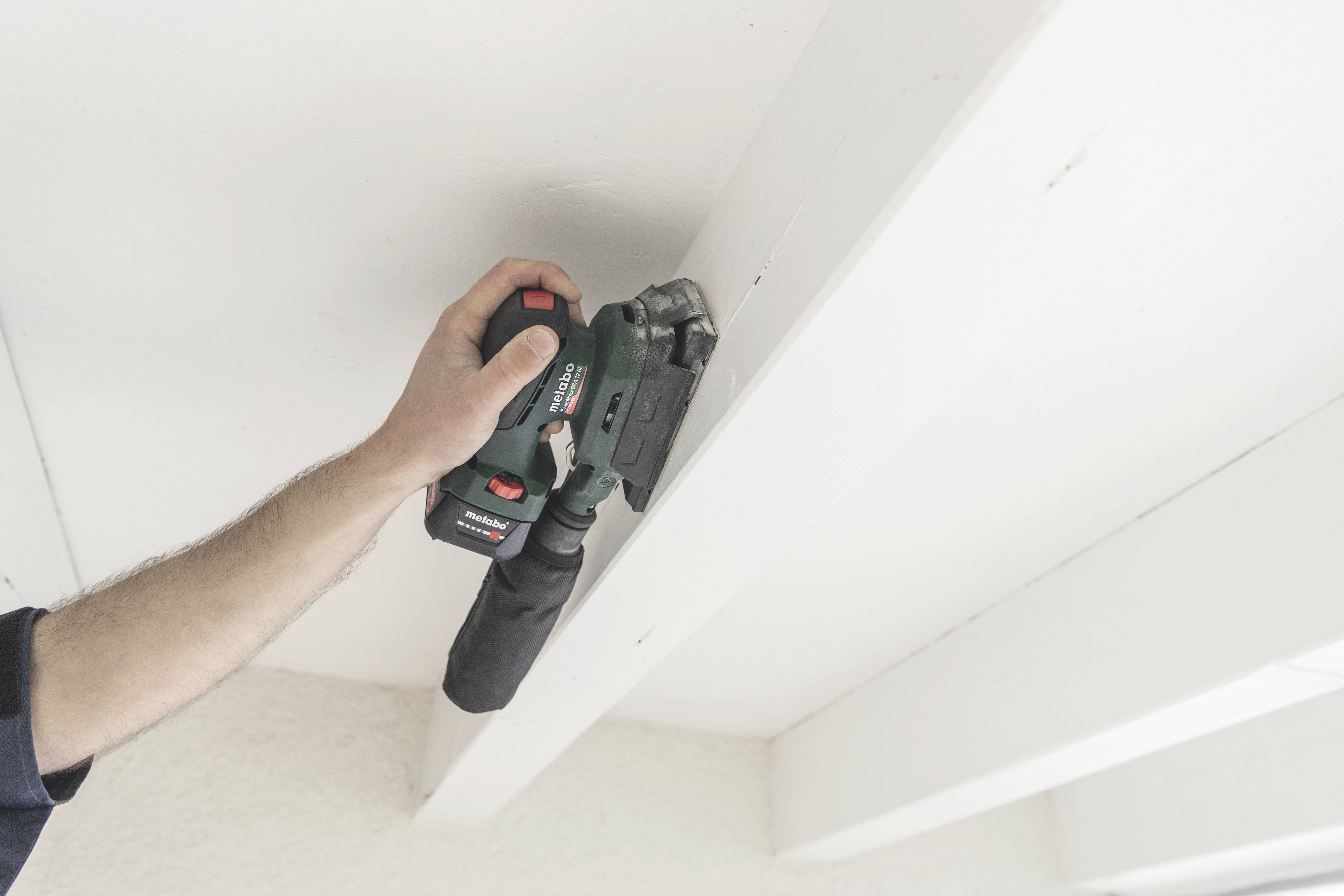 Eine Hand hält ein elektrisches Schleifgerät, das auf einem Holzbalken arbeitet, um die Oberfläche zu glätten.