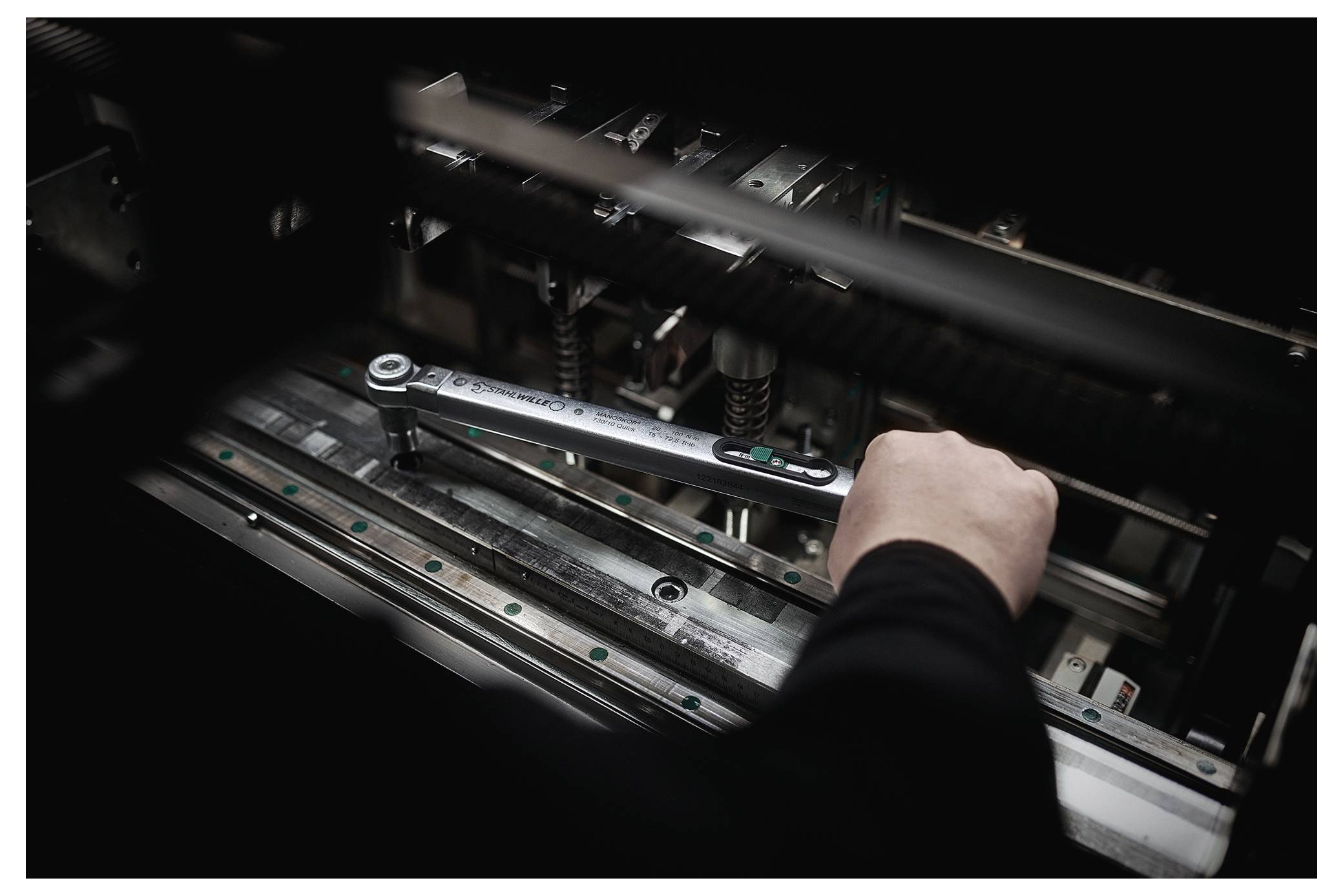 Eine Person nutzt einen großen Schraubenschlüssel, um Maschinenkomponenten zu justieren, was Wartungsarbeiten an Industrieanlagen hervorhebt.