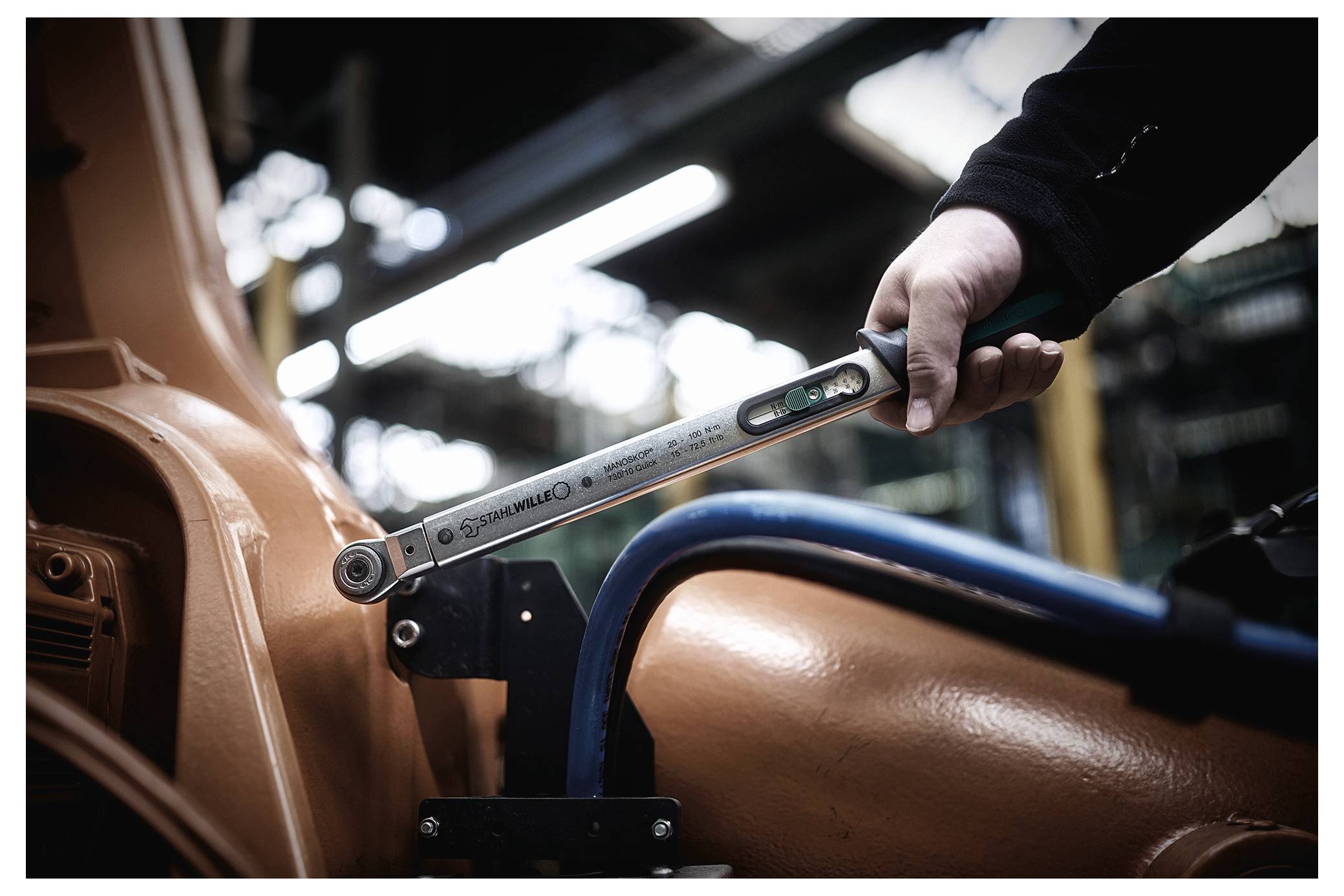 Eine Person verwendet einen Drehmomentschlüssel an Industrieausrüstung und stellt Maschinen in einer Fabrikumgebung ein oder montiert diese.