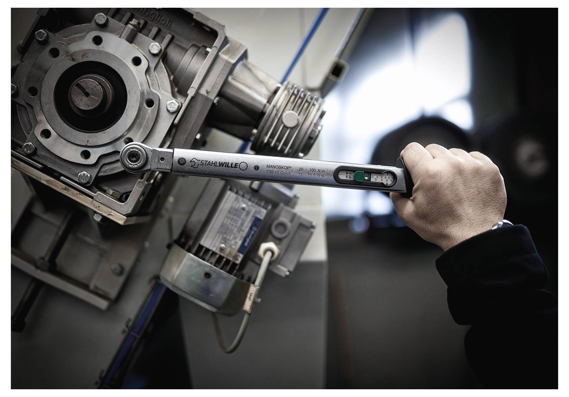 Eine Person nutzt einen Schraubenschlüssel, um einen großen Metallmechanismus in einer industriellen Umgebung einzustellen und hebt dabei manuelle mechanische Arbeit hervor.