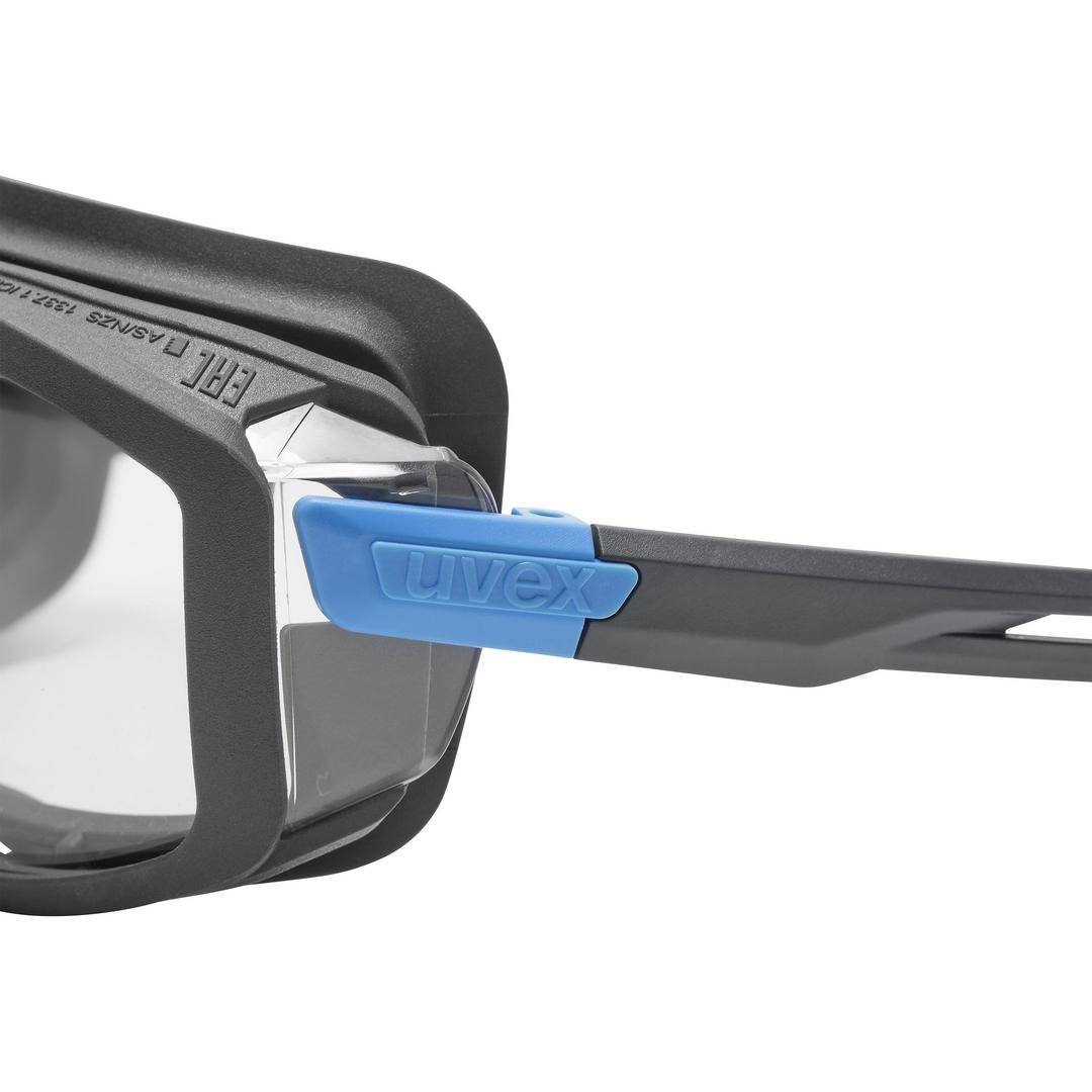 Eine Nahaufnahme einer Schutzbrille mit klarem Glas und blauem Akzentelement am Rahmen. Markennamen 'uvex' sichtbar.