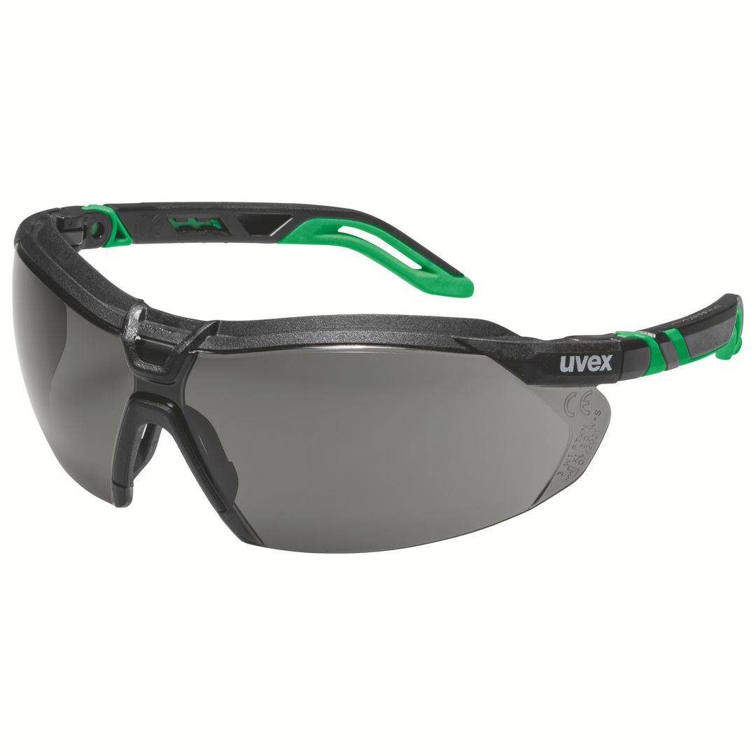 Graue Schutzbrille mit schwarzem Rahmen und grünen Akzenten. Marke 'uvex' auf dem rechten Bügel sichtbar.