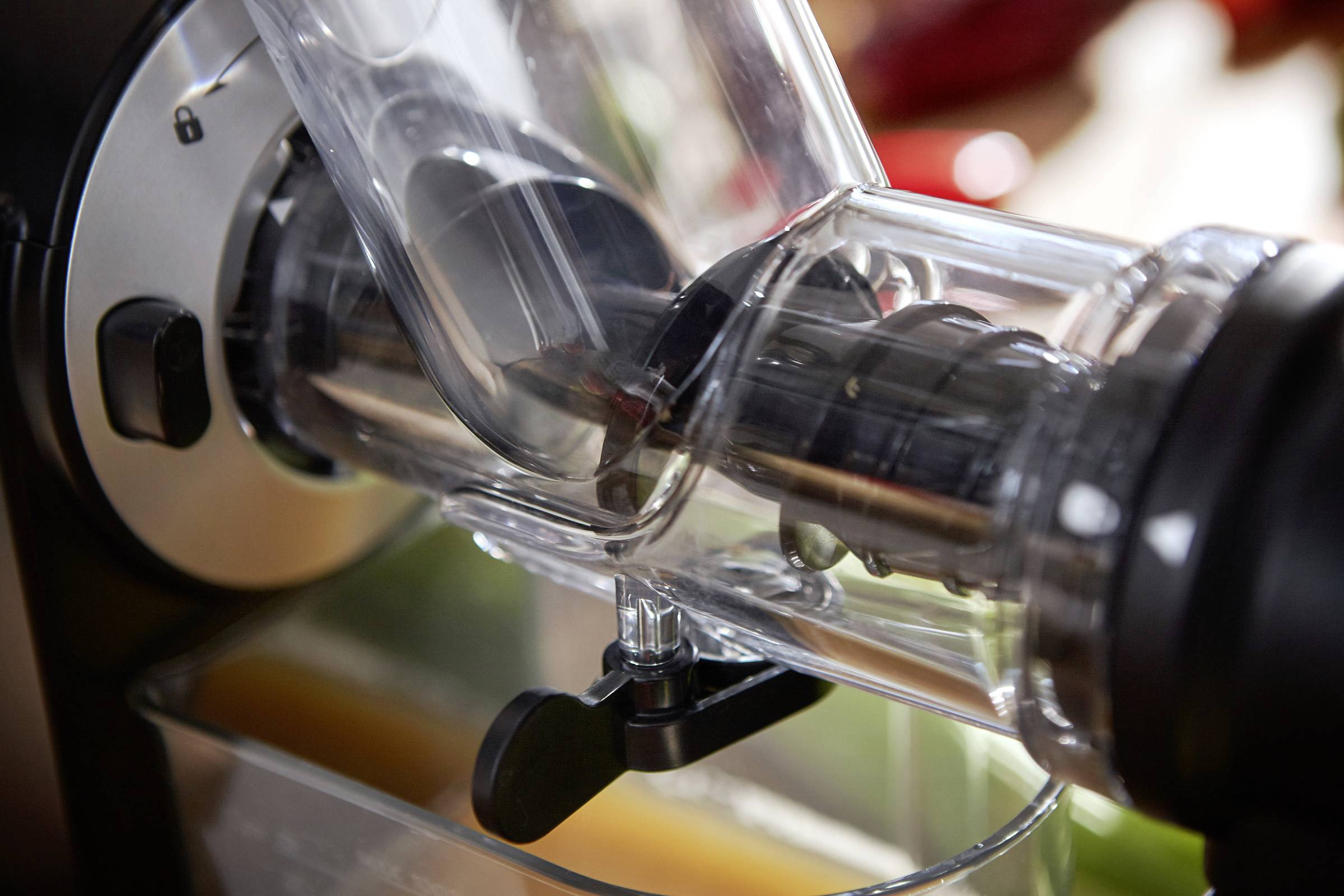 Nahaufnahme eines Entsafters während des Gebrauchs. Klarer Plastikbehälter mit Saftauslauf. Frisches Obst wird zu Saft verarbeitet.