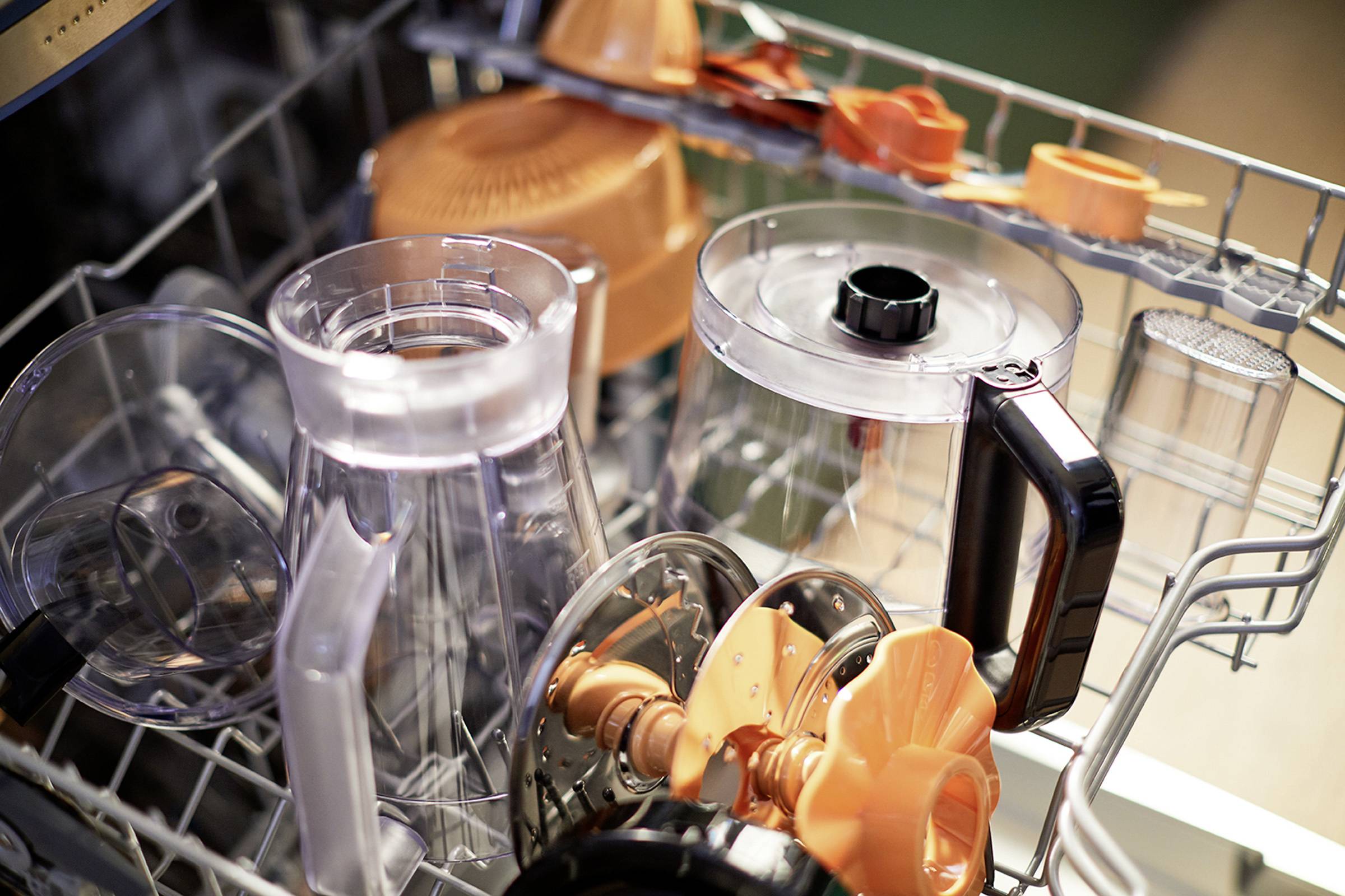 Spülmaschine mit diversen Geschirrteilen, darunter durchsichtige und orangefarbene Behälter sowie Aufsätze.