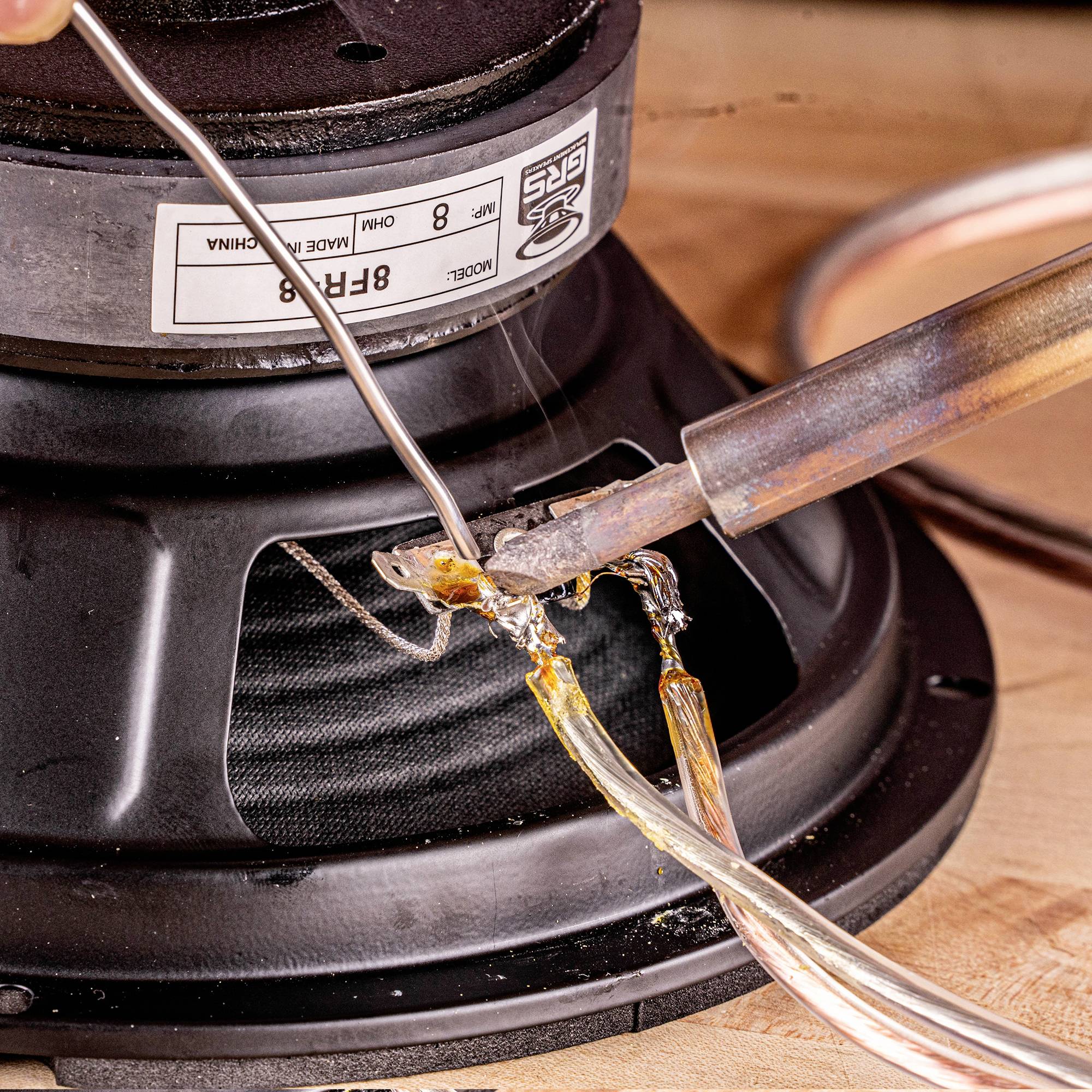 Lötkolben verbindet Kabel mit Lautsprechermembran, Nahaufnahme. Handwerksarbeit, elektronische Reparatur.