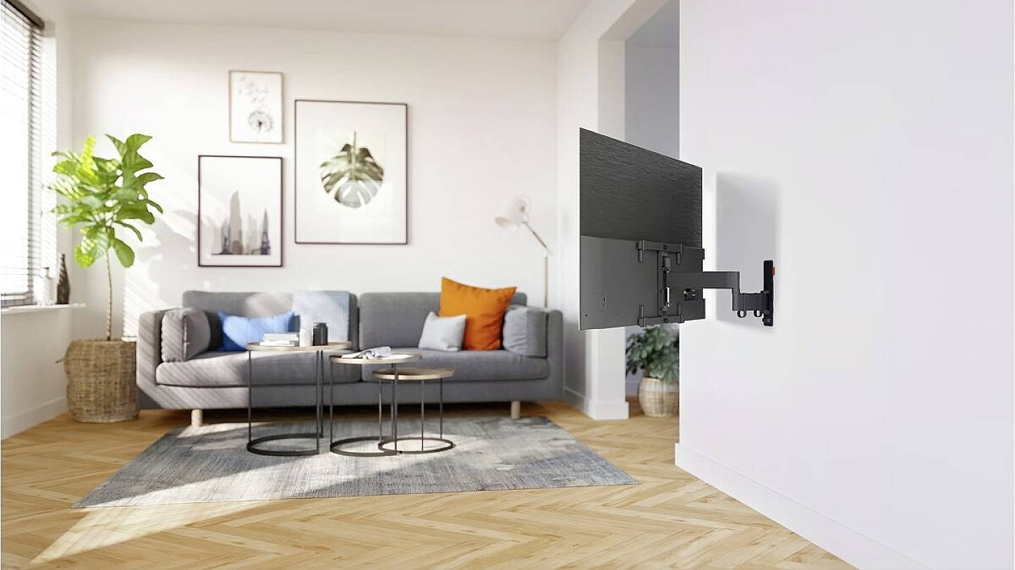 Ein modernes Wohnzimmer mit grauem Sofa, bunten Kissen und schwebendem Fernseher an der Wand. Pflanze und Kunstwerke zur Dekoration.