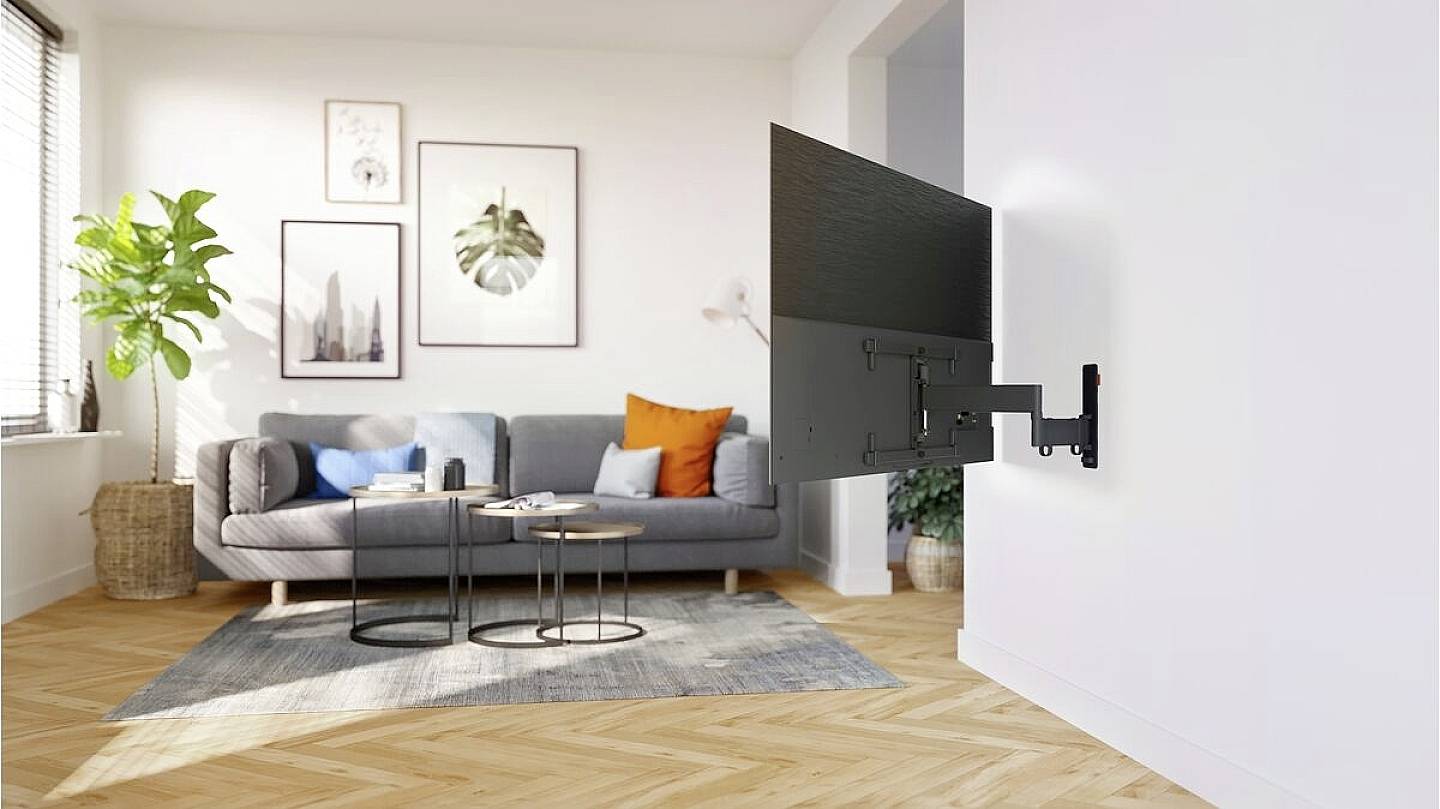 Wandhalterung mit schwenkbarem Flachbildfernseher in modernem Wohnzimmer mit grauem Sofa, Pflanzen und hellem Holzfußboden.