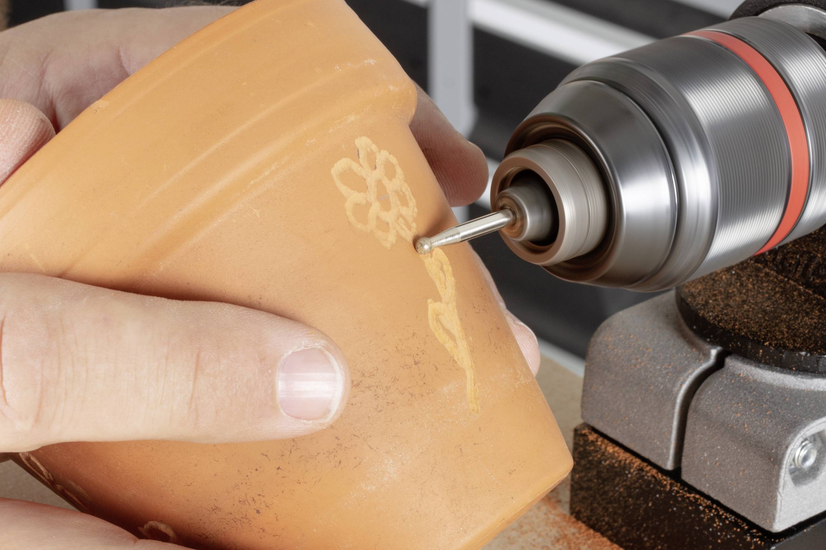 Eine Person graviert mit einer rotierenden Schleifmaschine eine Blume in einen Terrakotta-Blumentopf.