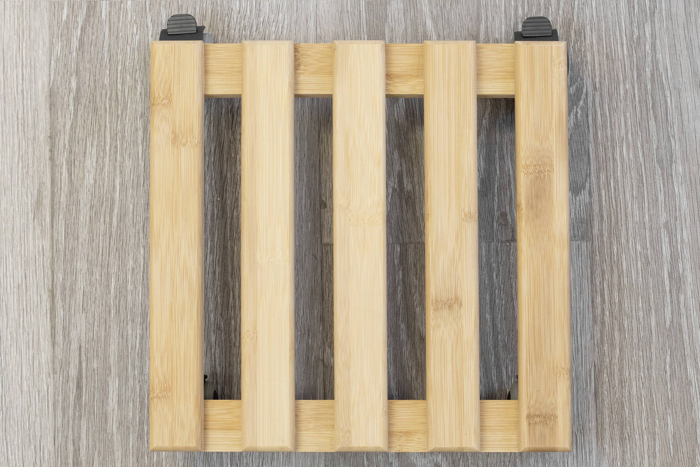 Ein quadratischer Untersetzer aus Holzlatten mit vier parallel angeordneten Streben auf einem hellgrauen Holzboden.