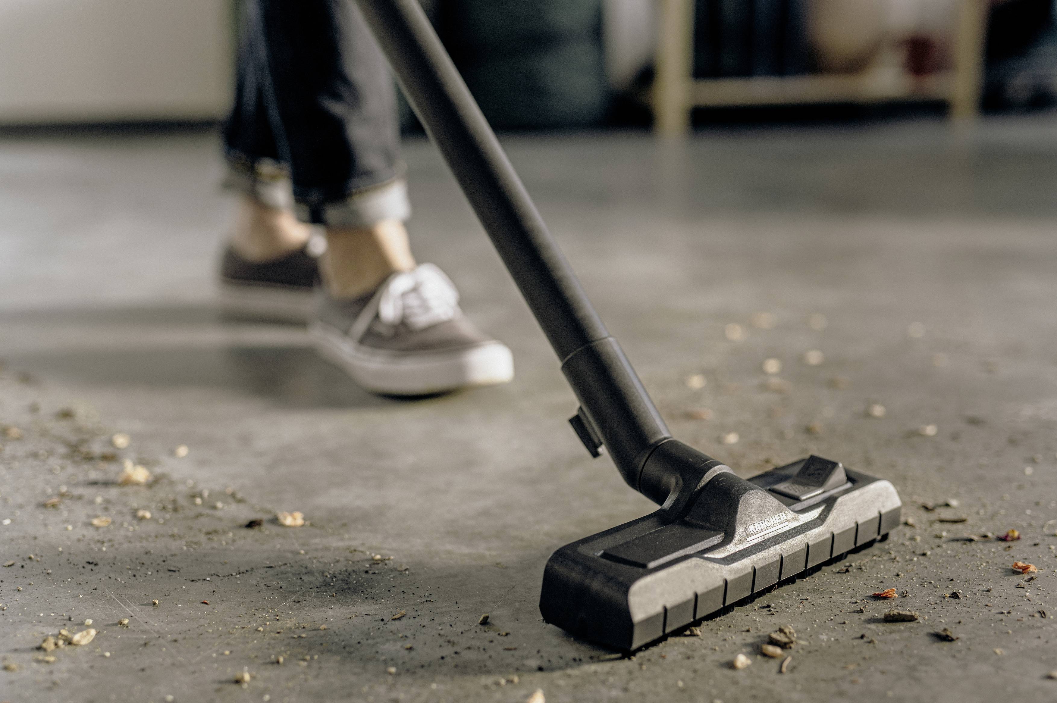Eine Person saugt mit einem Staubsauger schmutzigen Boden. Man sieht nur die Schuhe und den Staubsauger, während Verschmutzungen entfernt werden.