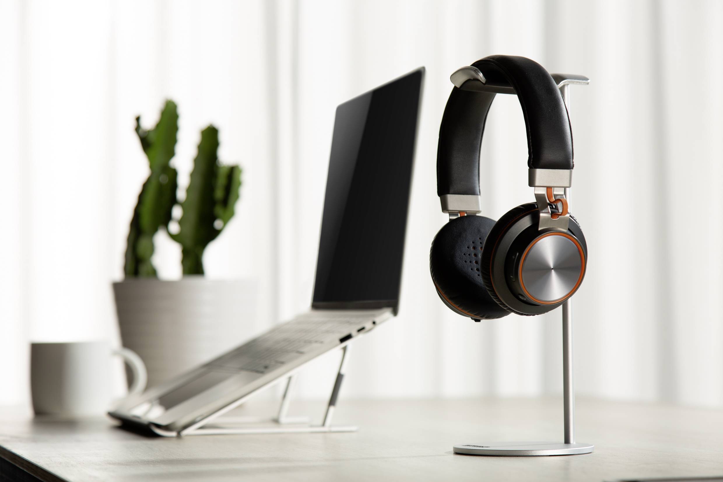 Ein Laptop steht auf einem Schreibtisch neben einem Paar Kopfhörer auf einem Ständer und einer Topfpflanze im Hintergrund.