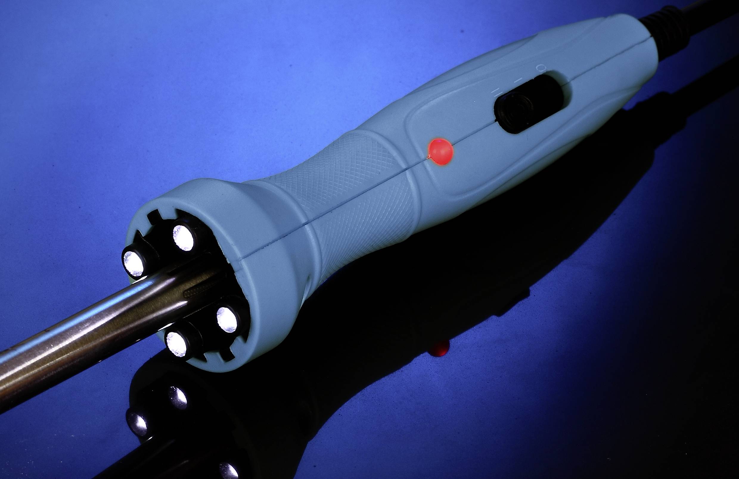 Ein Lötkolben mit blauem Griff liegt auf einer reflektierenden Oberfläche vor einem blauen Hintergrund.