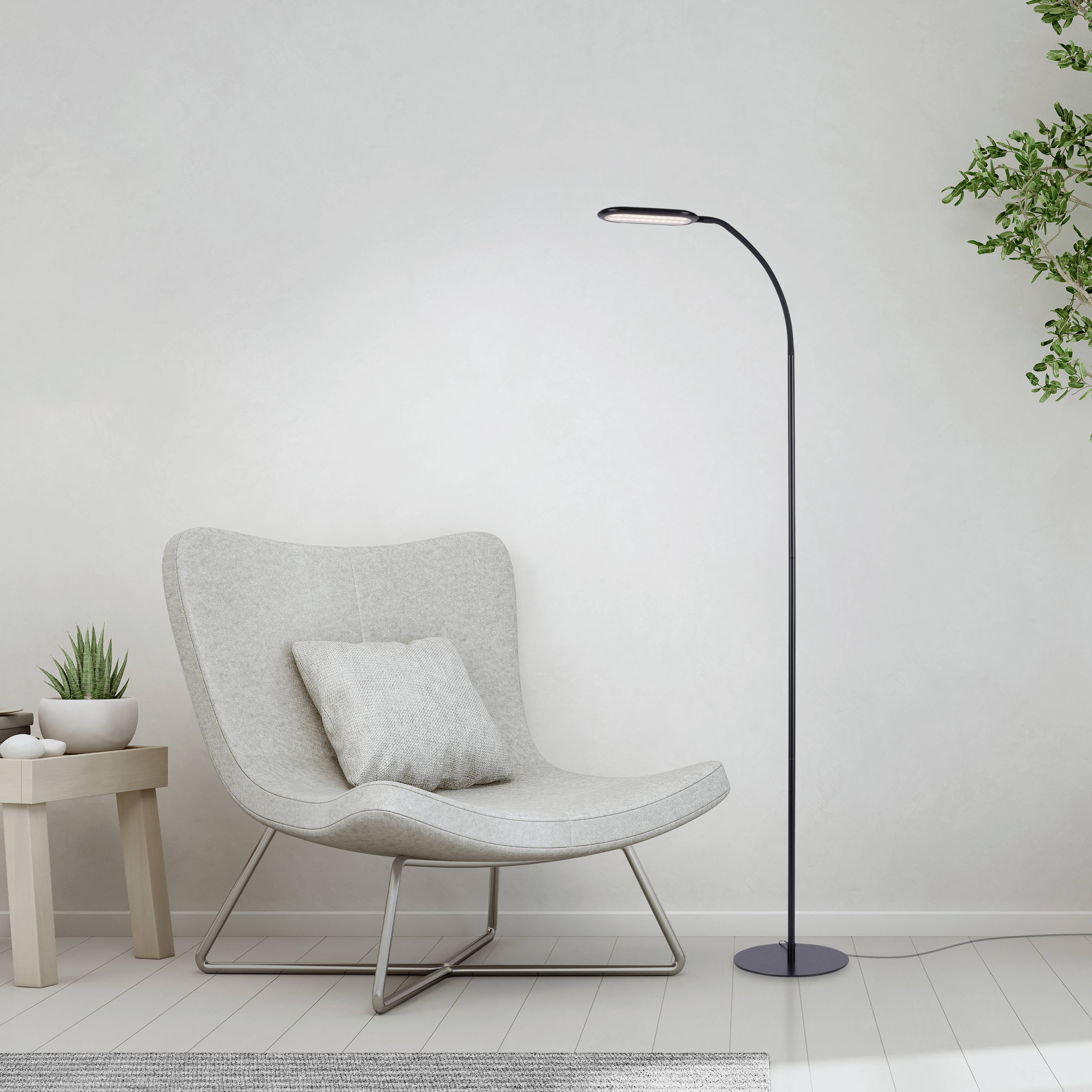 Ein moderner, weißer Sessel neben einer schlanken Stehlampe in einem minimalistisch eingerichteten Raum mit Pflanzen und Holztisch.