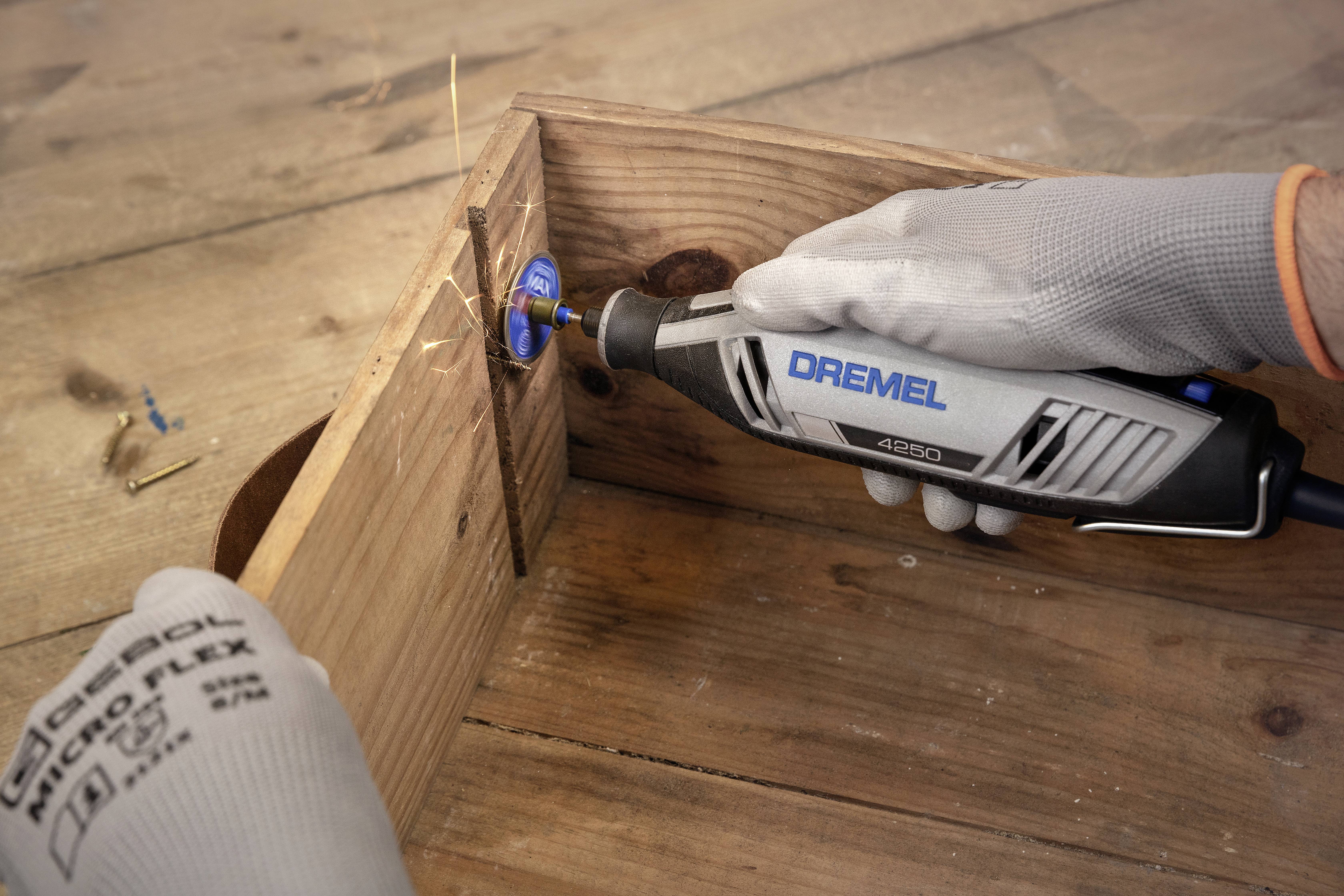 Eine Person arbeitet mit einem Dremel-Werkzeug an einem Holzobjekt. Funken fliegen beim Schleifen. Handschuhe schützen die Hände.