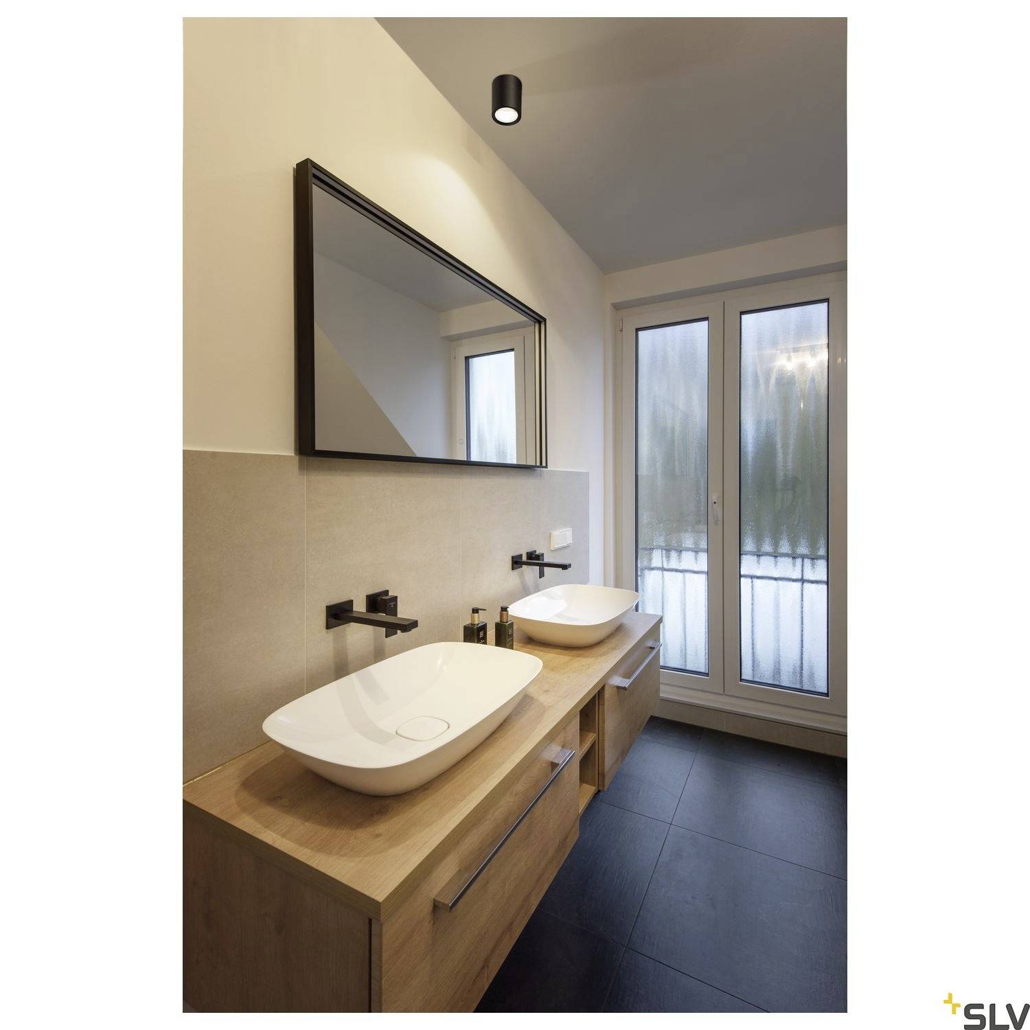 Modernes Badezimmer mit zwei weißen Waschbecken auf Holzunterschränken, großem Spiegel darüber und bodentiefem Fenster rechts.