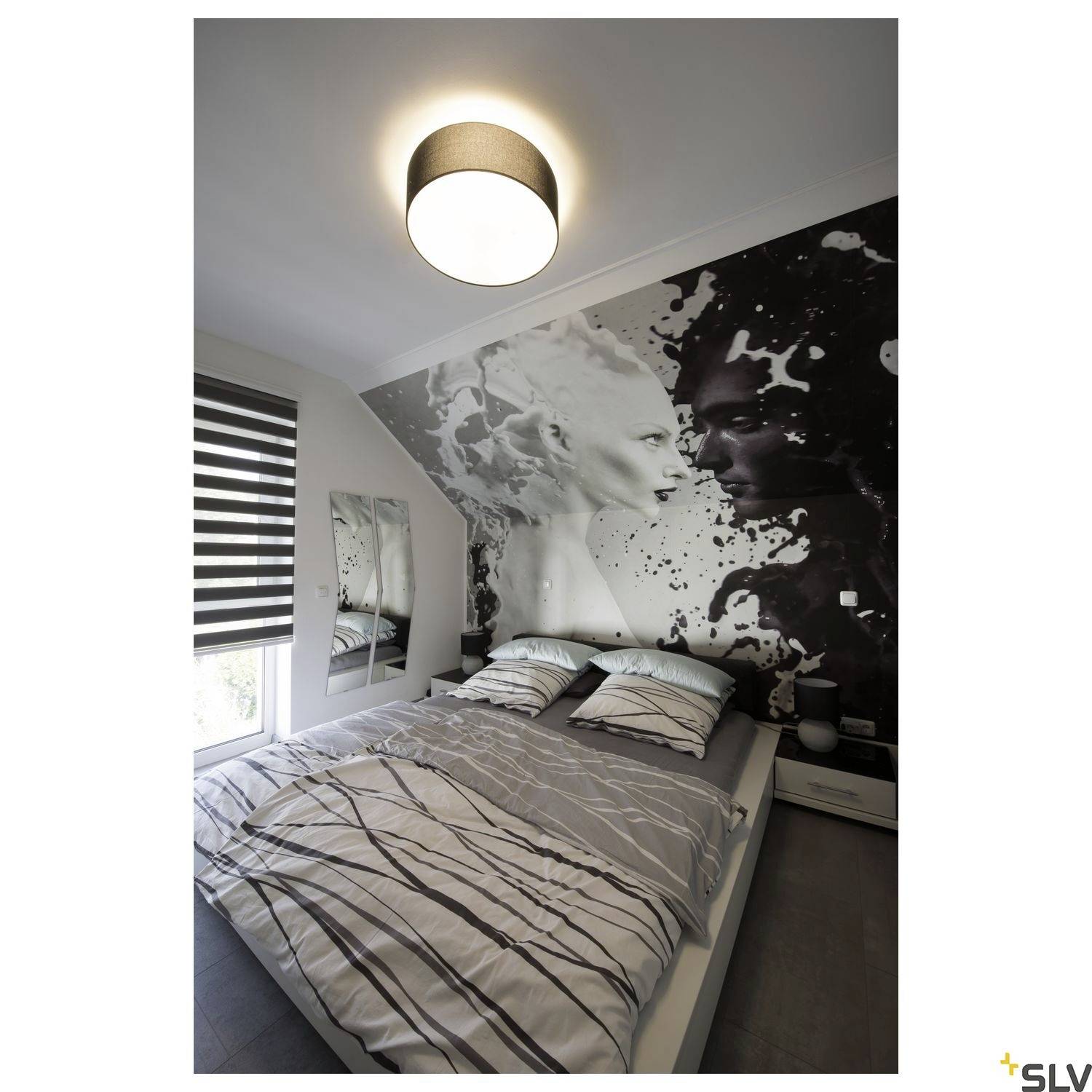 Ein modernes Schlafzimmer mit einem großen Bett, gestreifter Bettwäsche und einer Wand mit Kunstmotiv einer Frau in Schwarz-Weiß-Design.