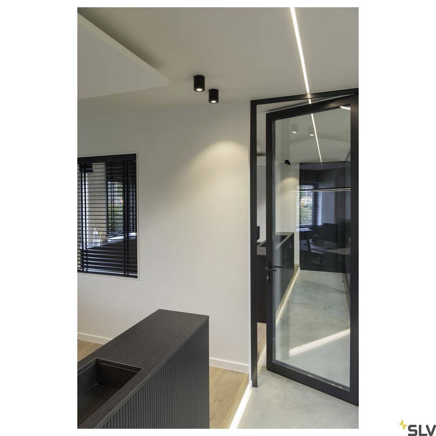 Moderne Innenraumgestaltung mit Glaswand, schwarzen Akzenten und minimalistischer Beleuchtung in einem Büroraum.