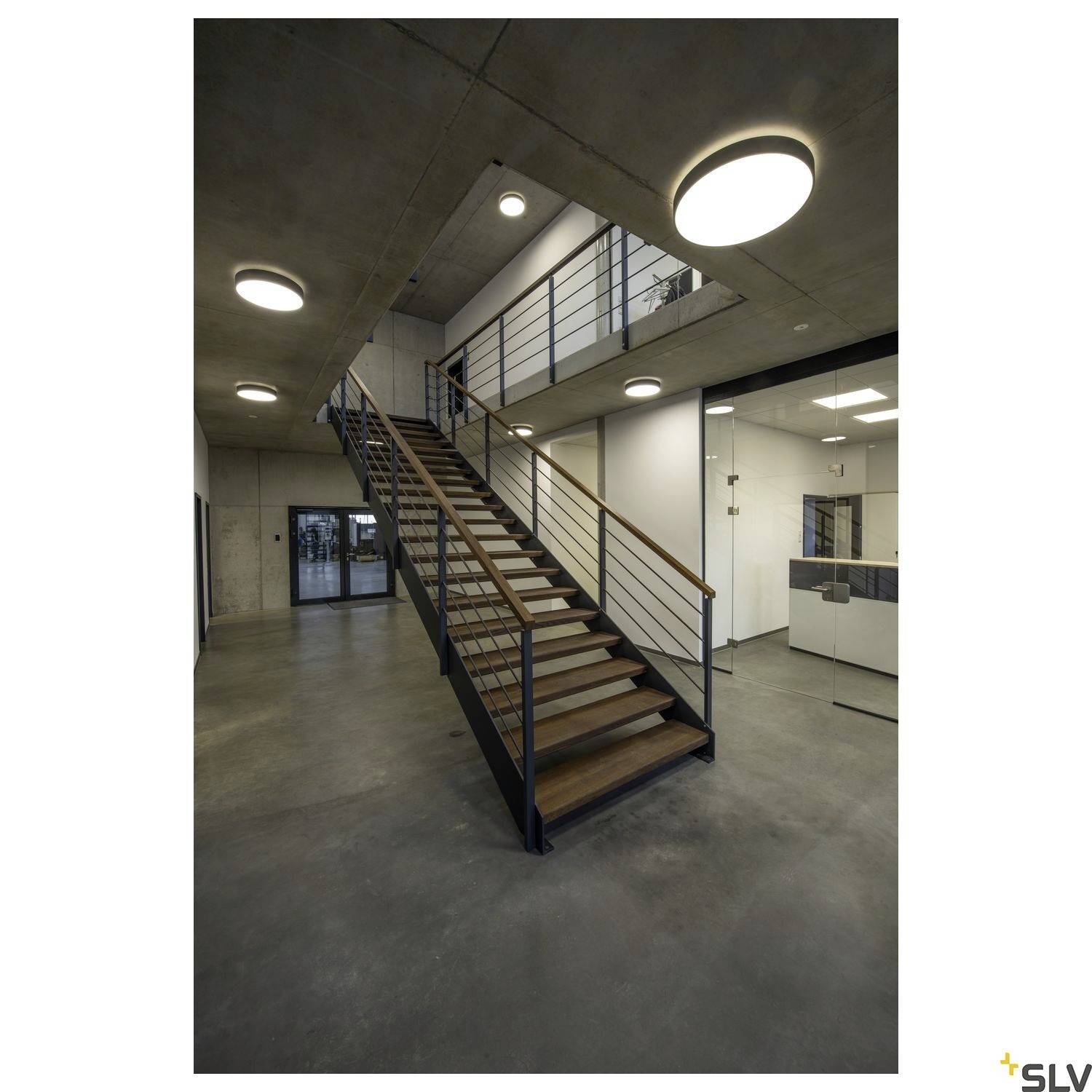 Eine moderne, minimalistische Treppe in einem Gebäude mit Betonwänden und mehreren runden, an der Decke montierten Leuchten.