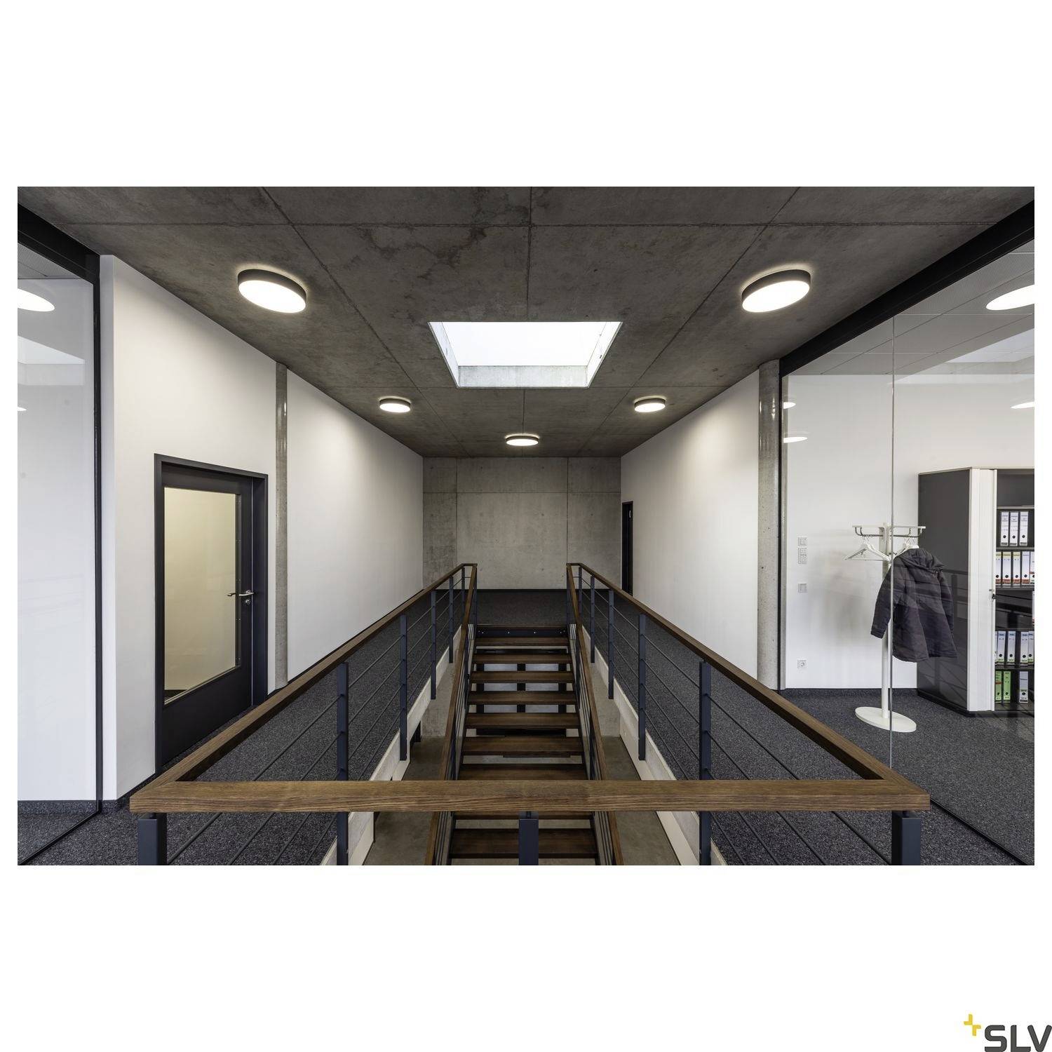 Ein modernes Büro, Flur mit Metallgeländer und Holzhandläufen. Die Decke hat runde Lampen und ein Oberlicht. Rechts seitlich ein Kleiderständer.