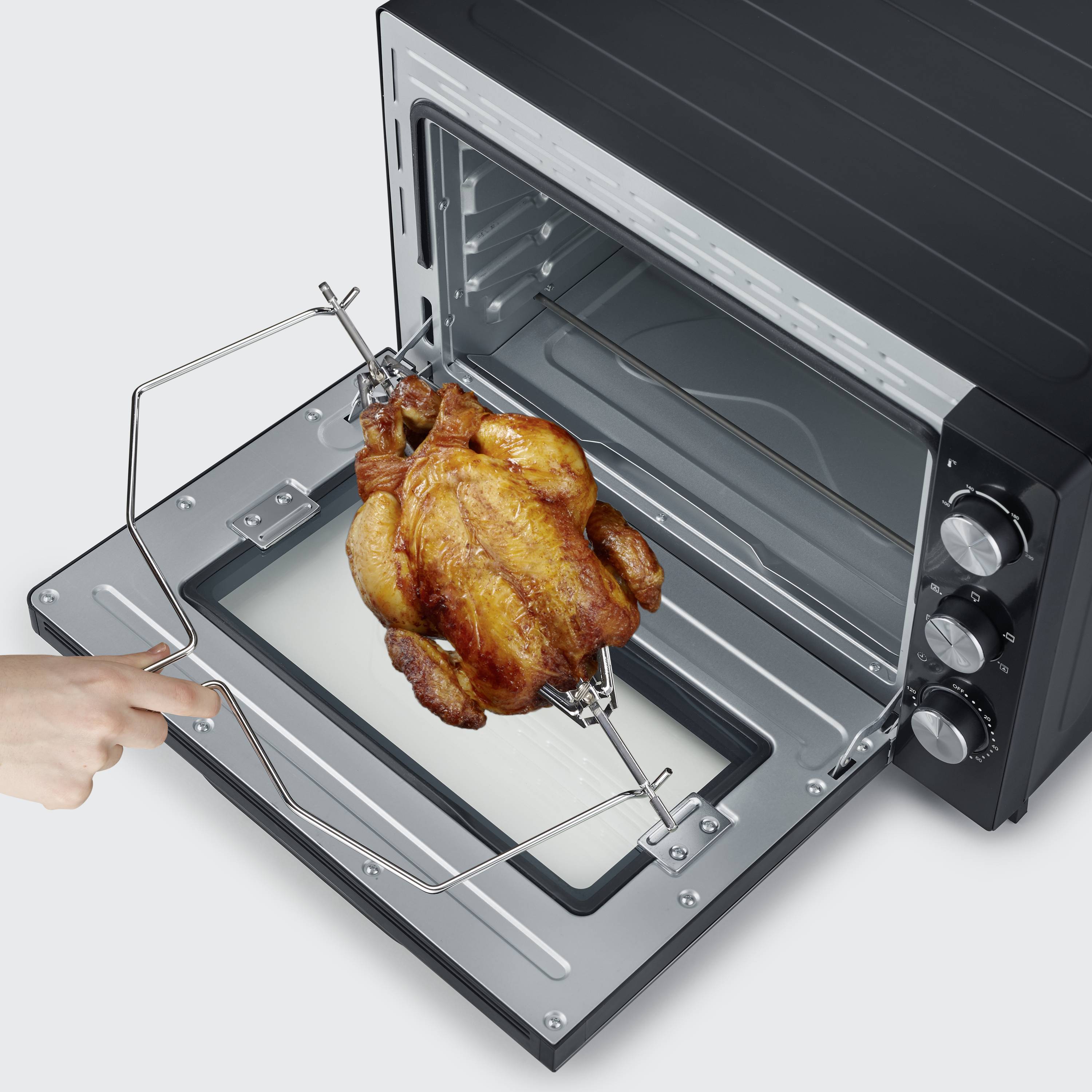 Eine Person nimmt einen gebratenen Hähnchenbraten aus einem schwarzen Ofen mit einem Handgriff heraus. Der Ofen ist offen.