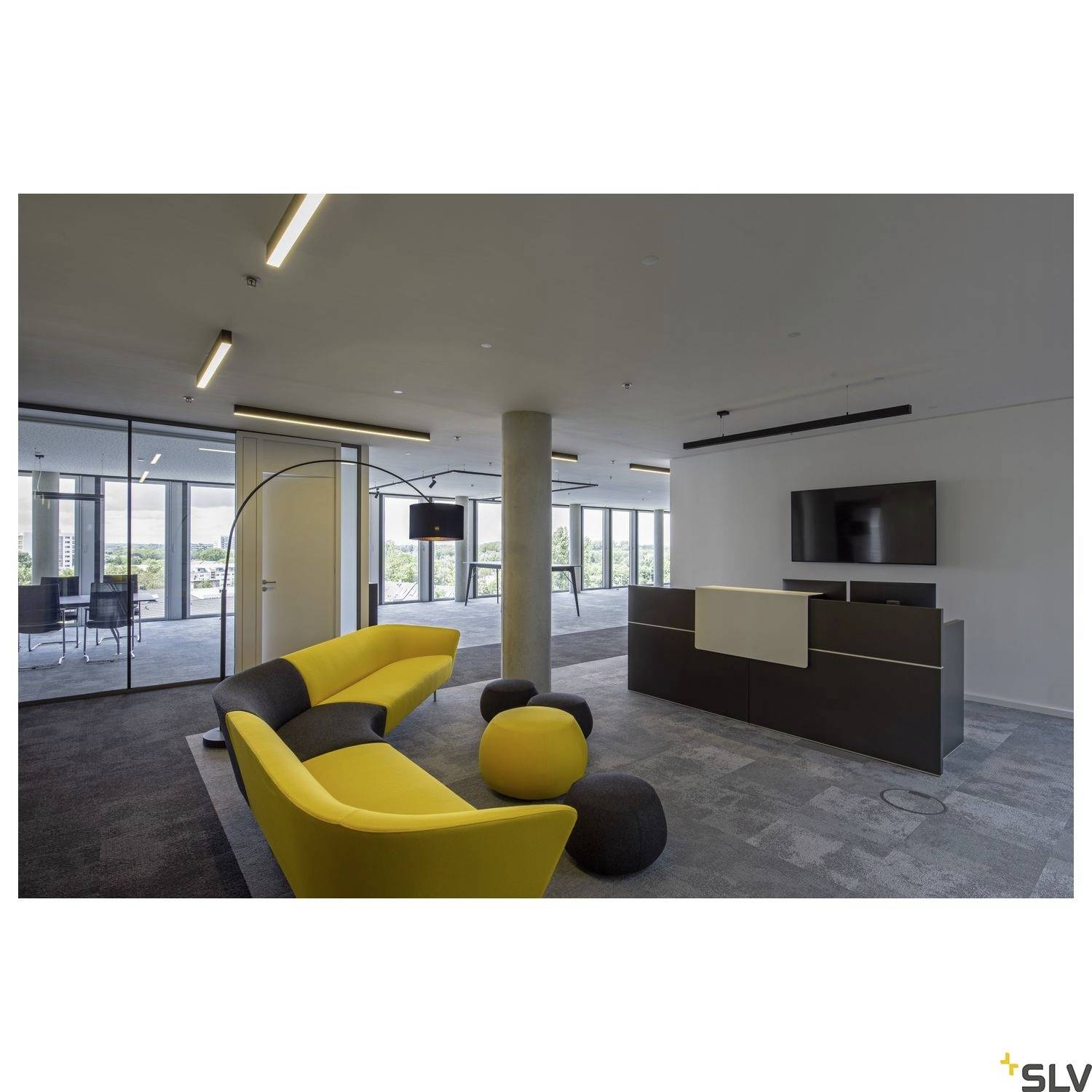 Modernes Büro mit gelben Sofas, grauen Teppichen, Tisch mit Stühlen im Hintergrund und einem Fernseher an der Wand. Großzügige Fenster.