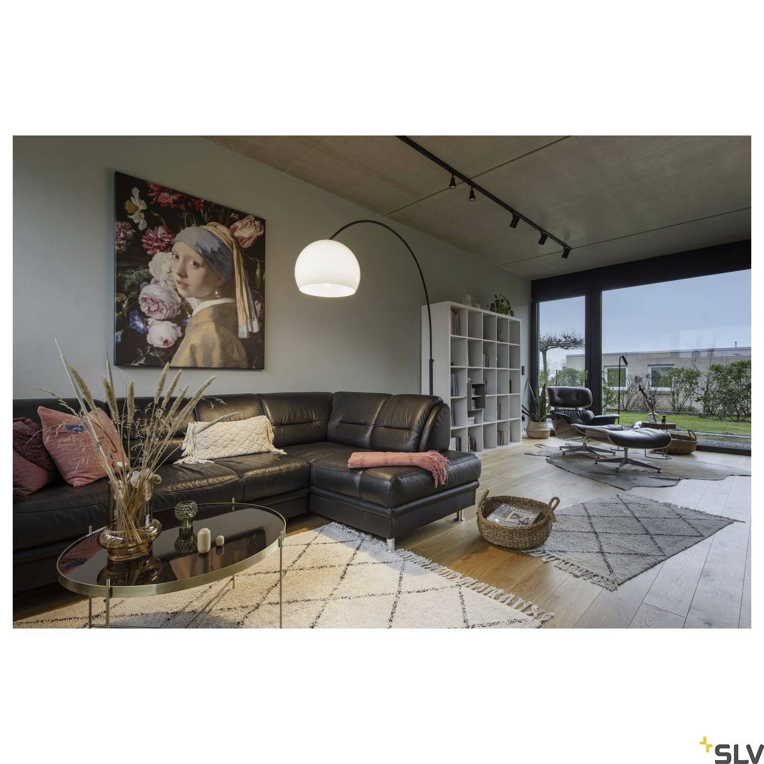 Ein modernes Wohnzimmer mit schwarzen Ledersofas, einem runden Glastisch, einem großen Gemälde, Regalen und einem Blick auf den Garten.