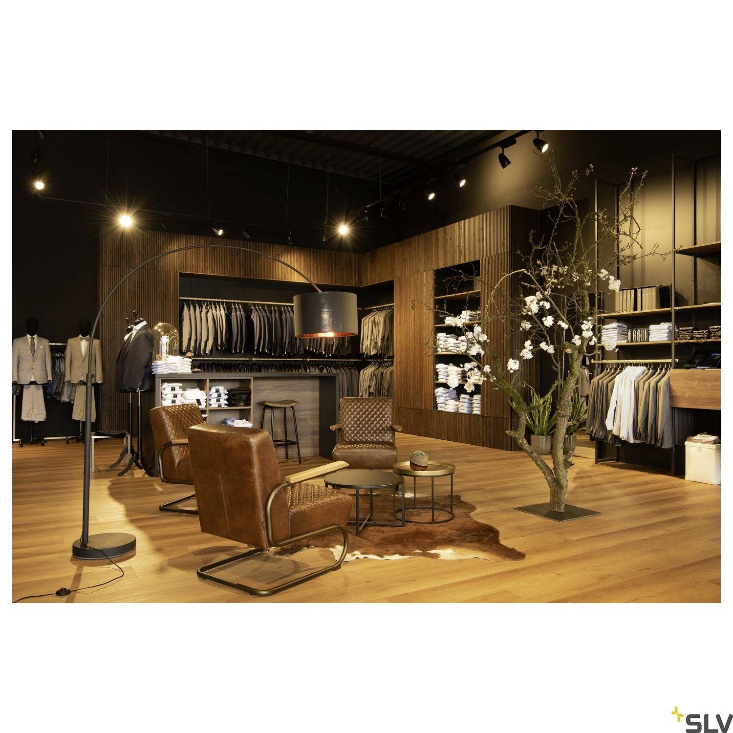 Ein stilvoller Bekleidungsladen mit modernen, braunen Ledersesseln, Holzregalen mit gefalteter Kleidung und eleganter Dekoration.