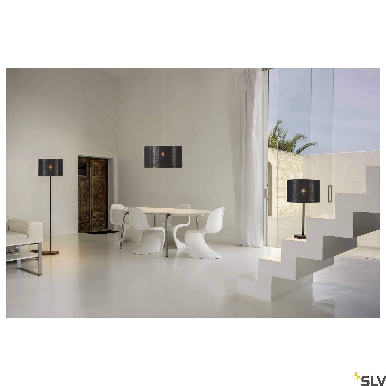 Moderne, minimalistische Innenaufnahme eines Wohnzimmers. Runde Tischgruppe mit weißen Stühlen, steile Treppe, große Fensterfront.