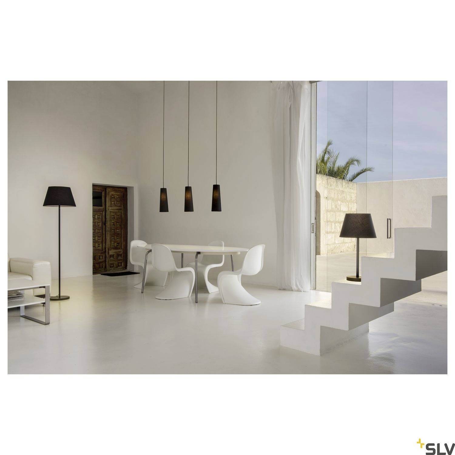 Ein modernes, minimalistisch eingerichtetes Wohnzimmer mit weißen Möbeln, einem Esstisch und einer Treppe vor einer großen Glasfassade.