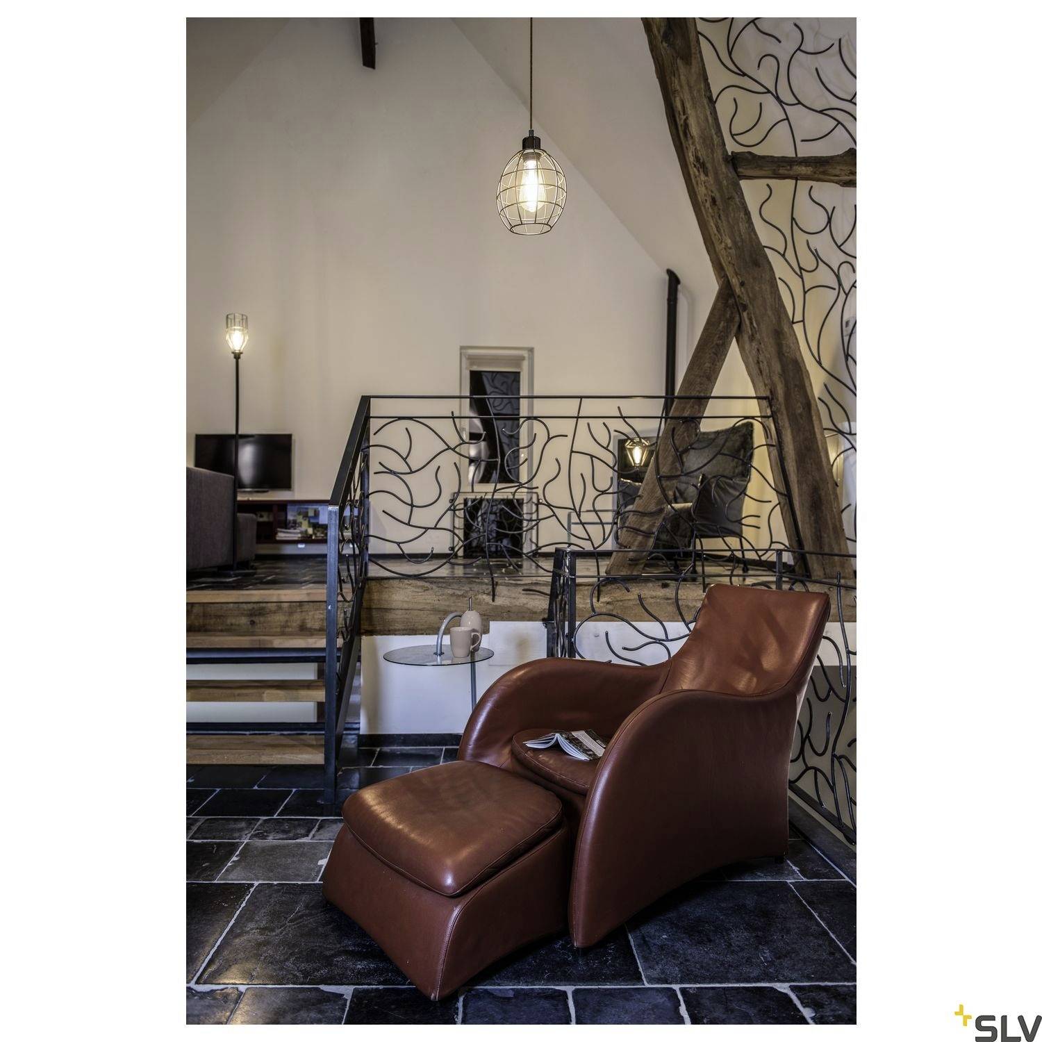 Ein gemütlicher Raum mit einem braunen Ledersessel, Lampen und Holzbalken. Ein Hauch von industriellem und modernem Design.