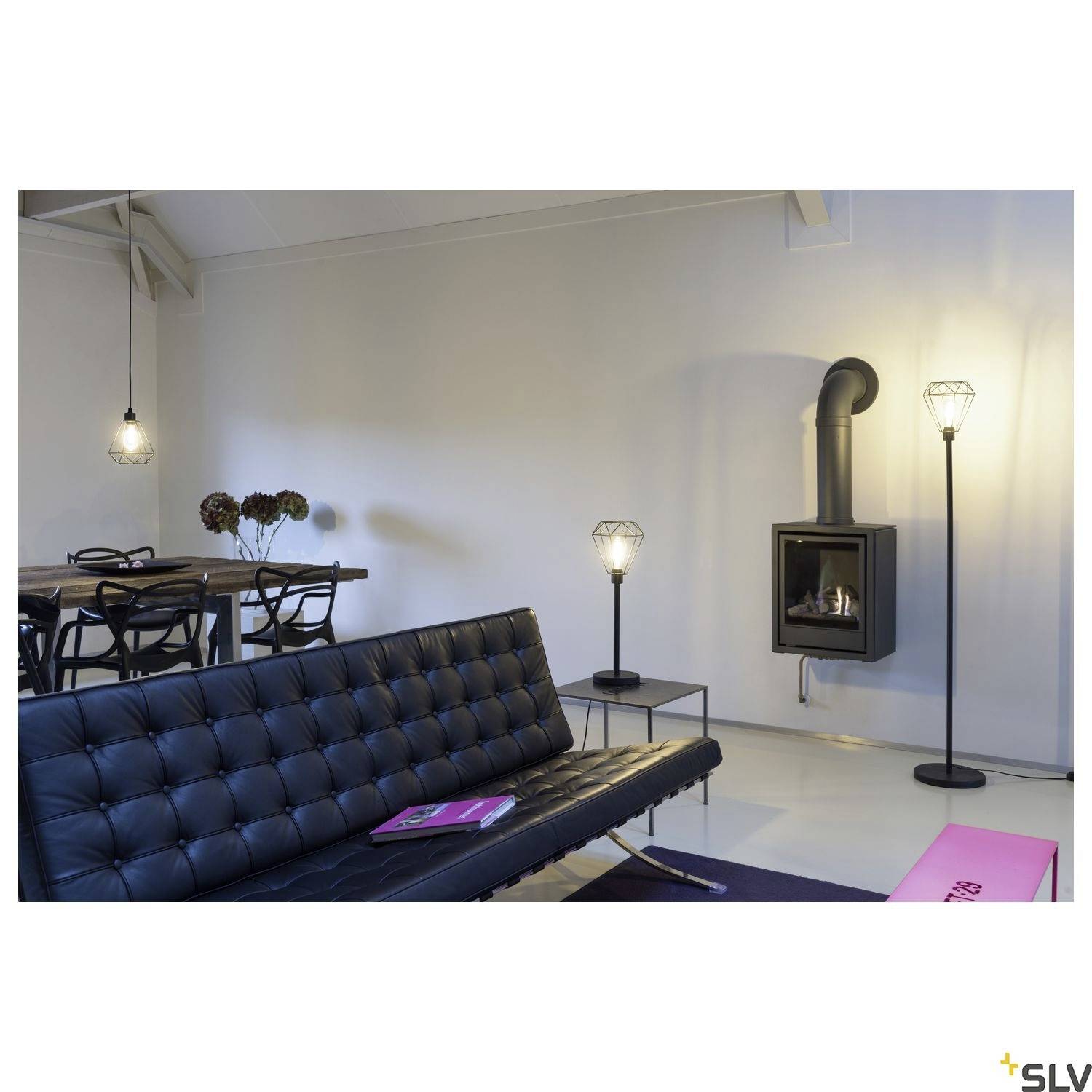 Ein modernes Wohnzimmer mit einem schwarzen Sofa, einem Kamin und einer Esstischgruppe. Die Beleuchtung ist stilvoll und minimalistisch.