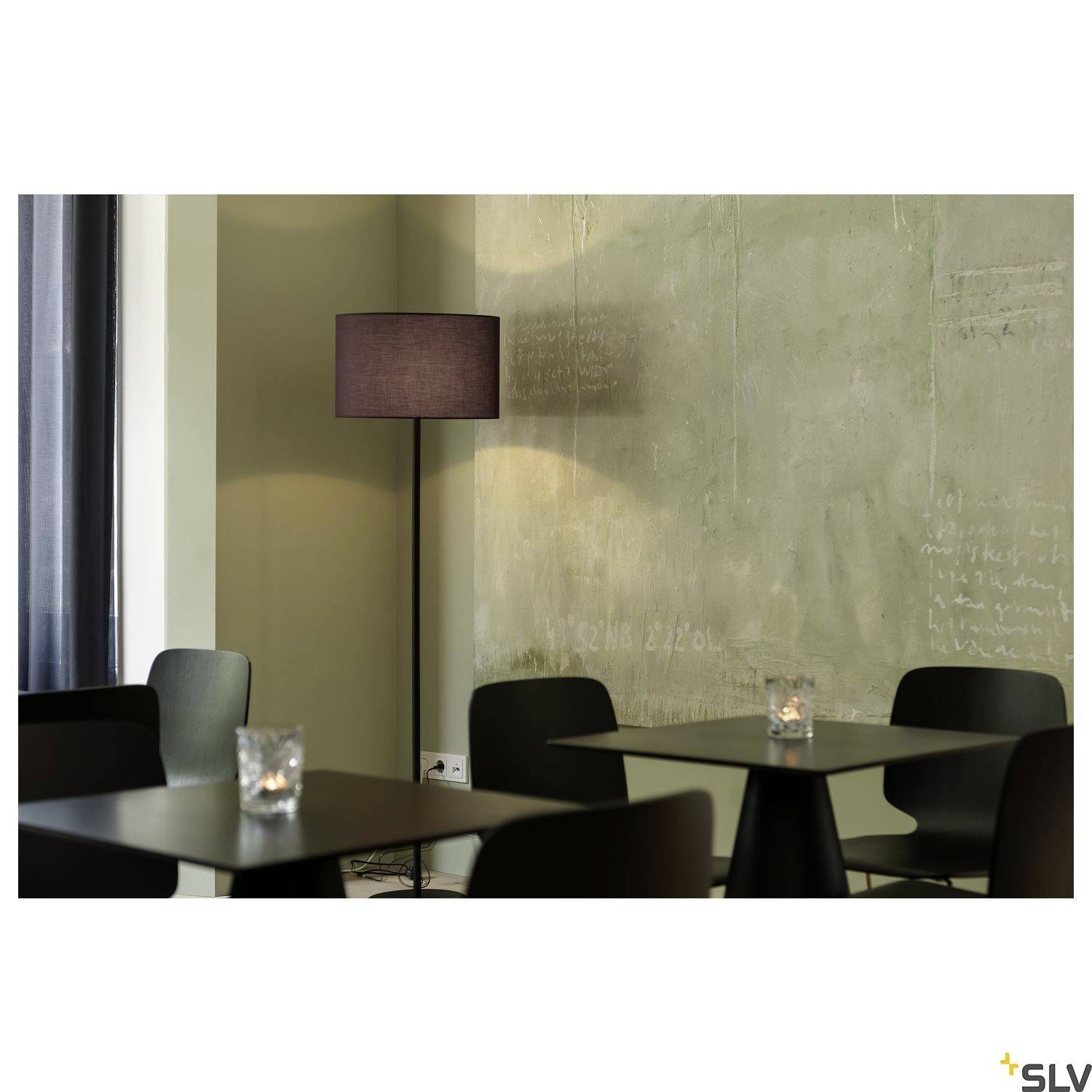 Ein gemütliches Café mit einem Stehlampe, die weiches Licht spendet. Dunkle Tische und Kerzen auf jedem Tisch schaffen eine entspannte Atmosphäre.