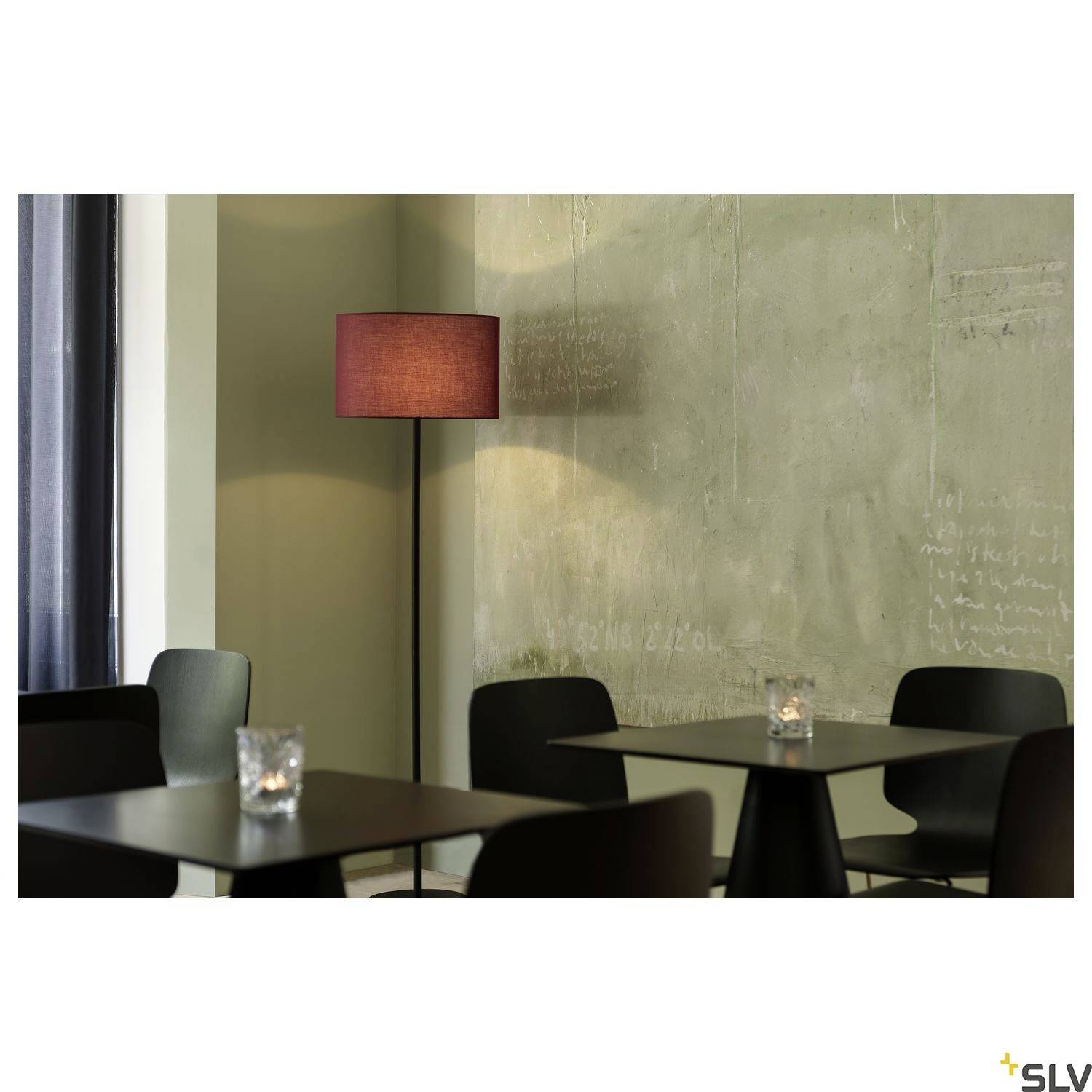 Ein modern eingerichtetes Café mit schwarzen Stühlen und Tischen, beleuchtet durch eine Stehlampe mit rotem Schirm an einer grauen Wand.