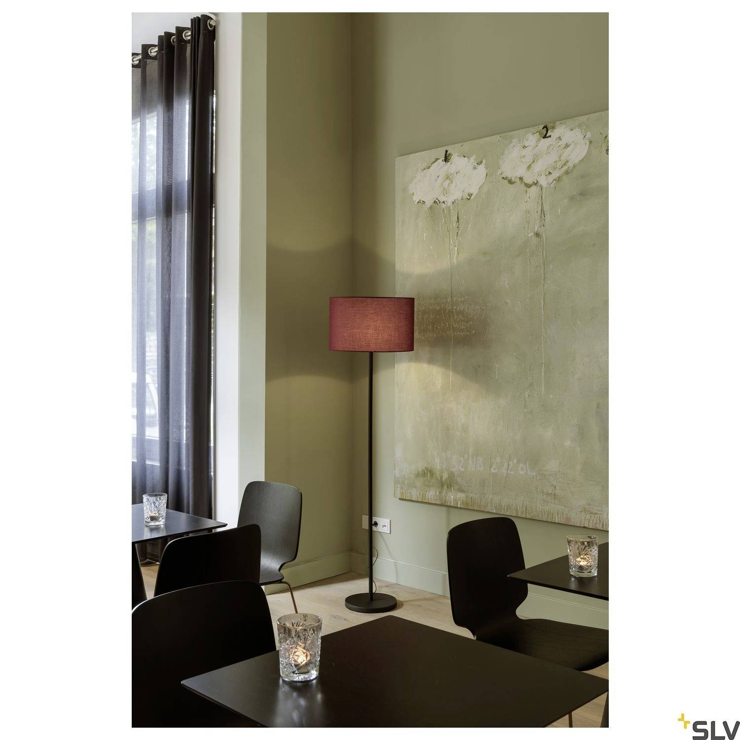 Ein Café mit moderner Einrichtung: vier schwarze Tische, eine Stehleuchte mit rotem Schirm und ein großes Gemälde an der Wand.