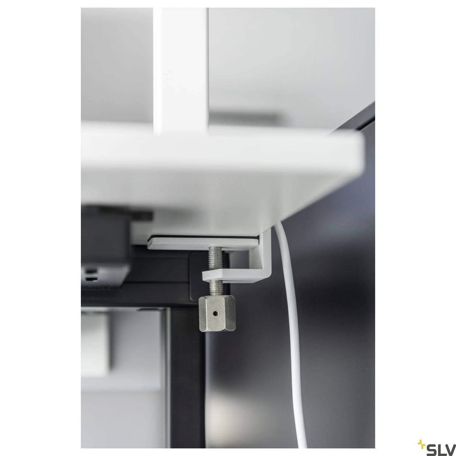 Ein weißes Regal wird mit einer Metallklammer an einer schwarzen Wand befestigt. Ein weißes Kabel hängt daneben herunter.