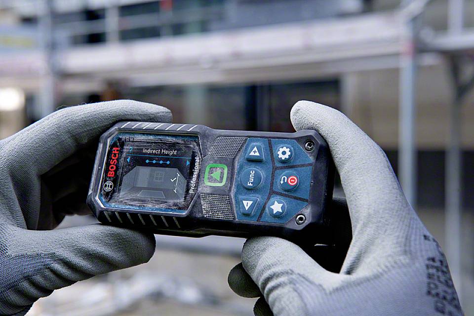 Eine Person mit grauen Arbeitshandschuhen hält ein digitales Bosch-Lasermessgerät, das zur Messung von Distanzen verwendet wird.
