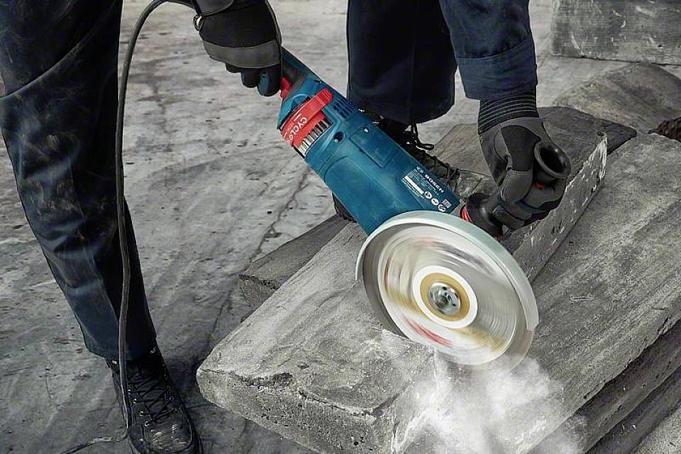 Eine Person schneidet mit einem elektrischen Winkelschleifer einen Betonblock. Funken sprühen, und Staub wird aufgewirbelt.