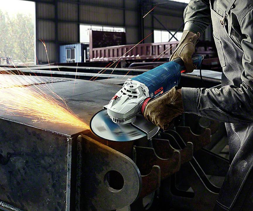 Arbeiter verwendet eine blaue Schleifmaschine, Funken fliegen. Szene in einer Fabrikhalle, Metallverarbeitung.