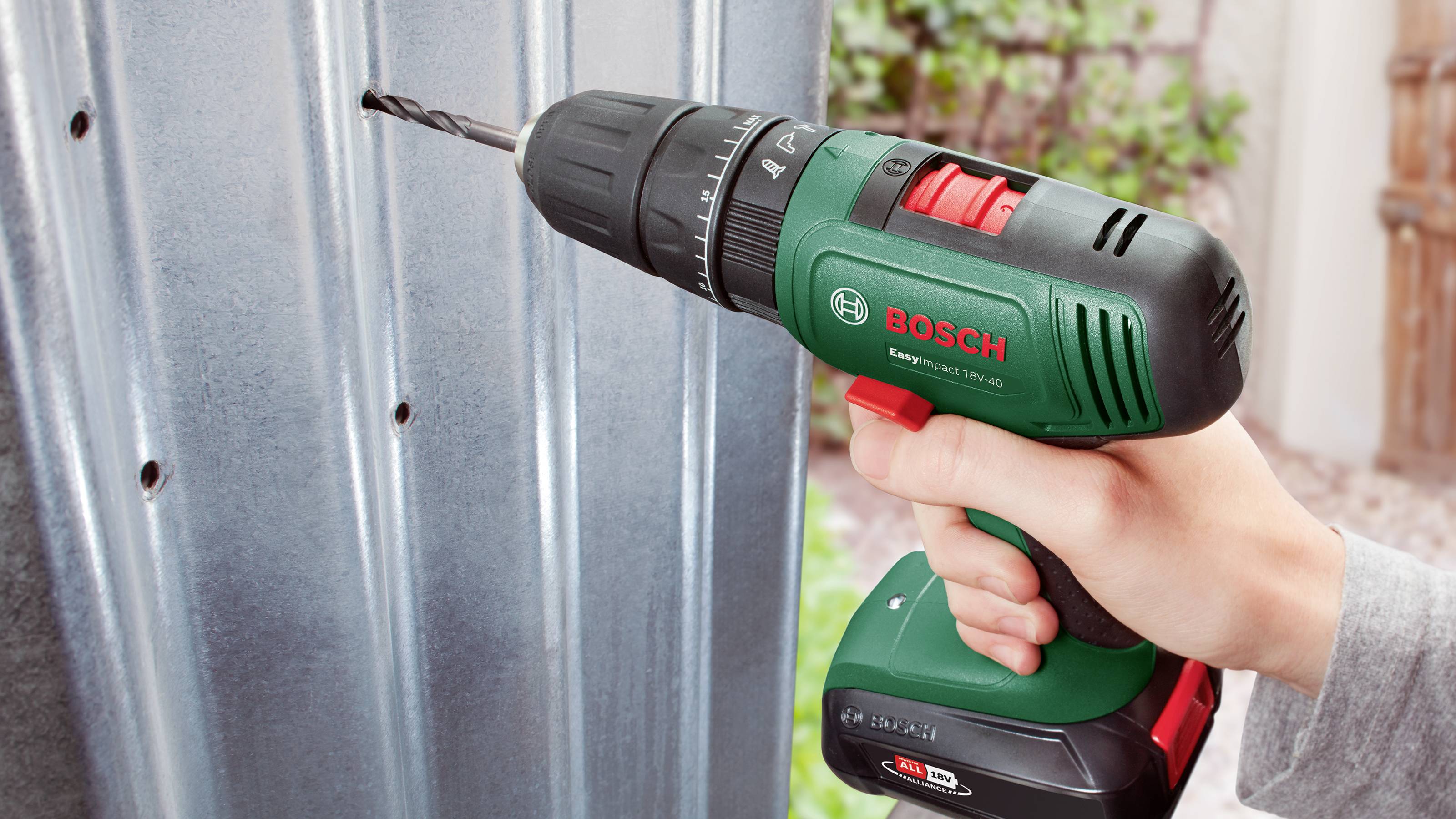 Eine Hand hält einen Bosch-Akkubohrschrauber und bohrt ein Loch in ein Metallblech.