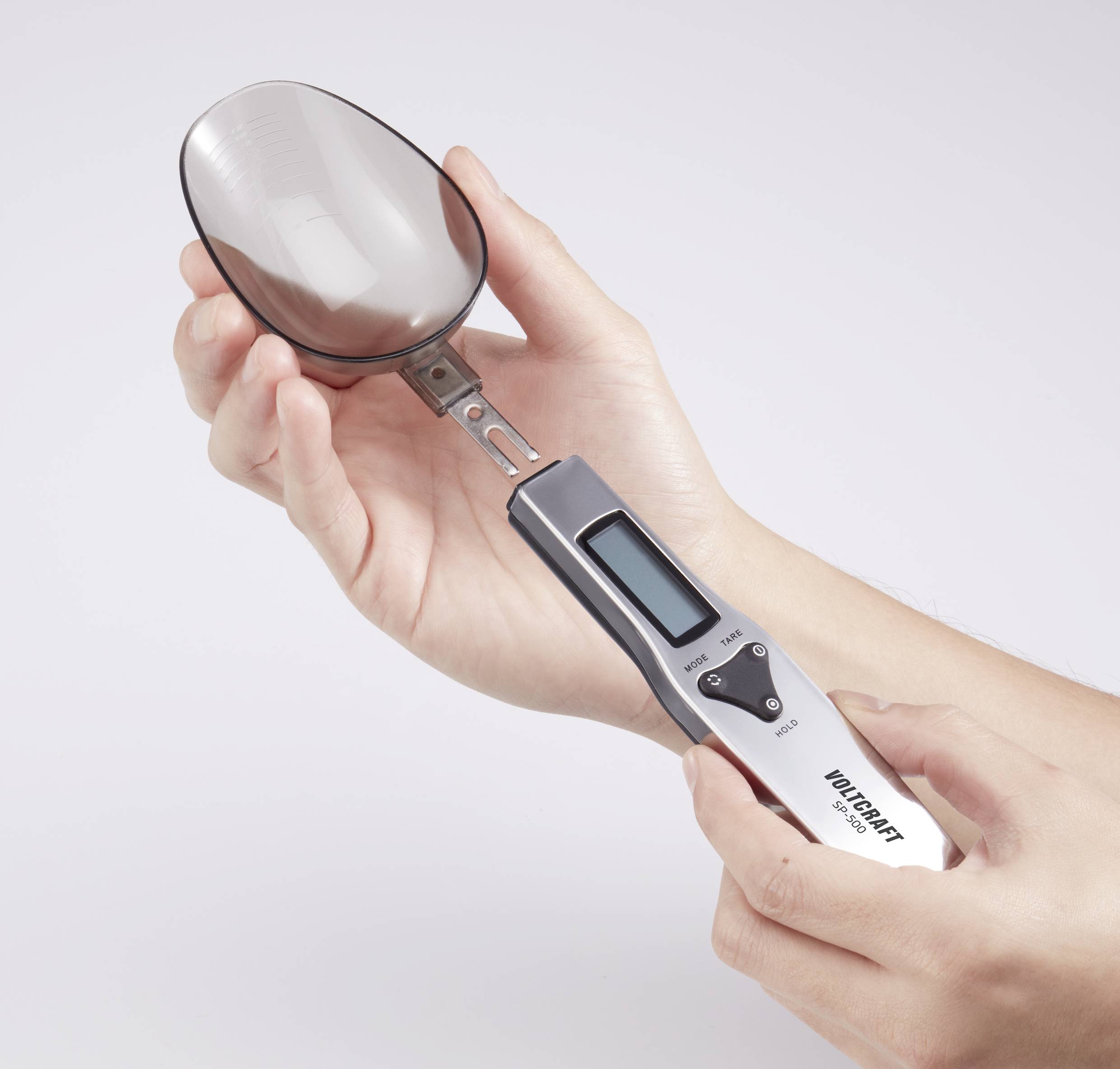Elektronische Löffelwaage mit einem Display, in beiden Händen gehalten. Sie zeigt Gewichtsmessung kleiner Mengen an.
