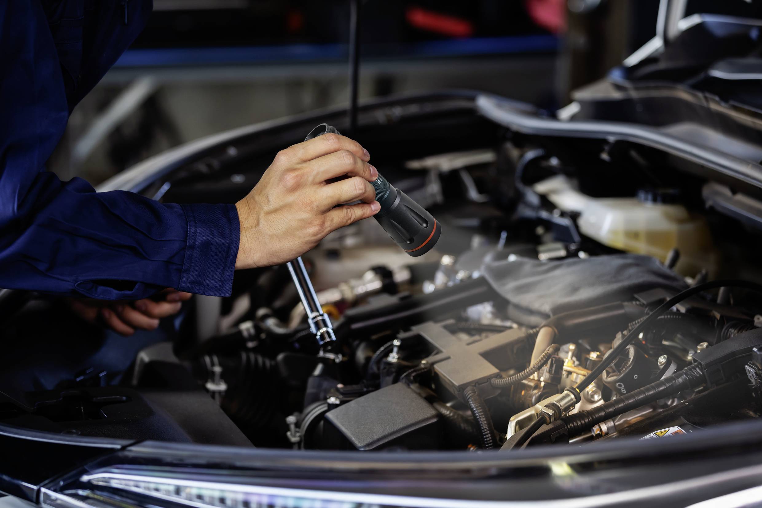 Mechaniker prüft Motor eines Autos mit einer Taschenlampe in der Werkstatt.