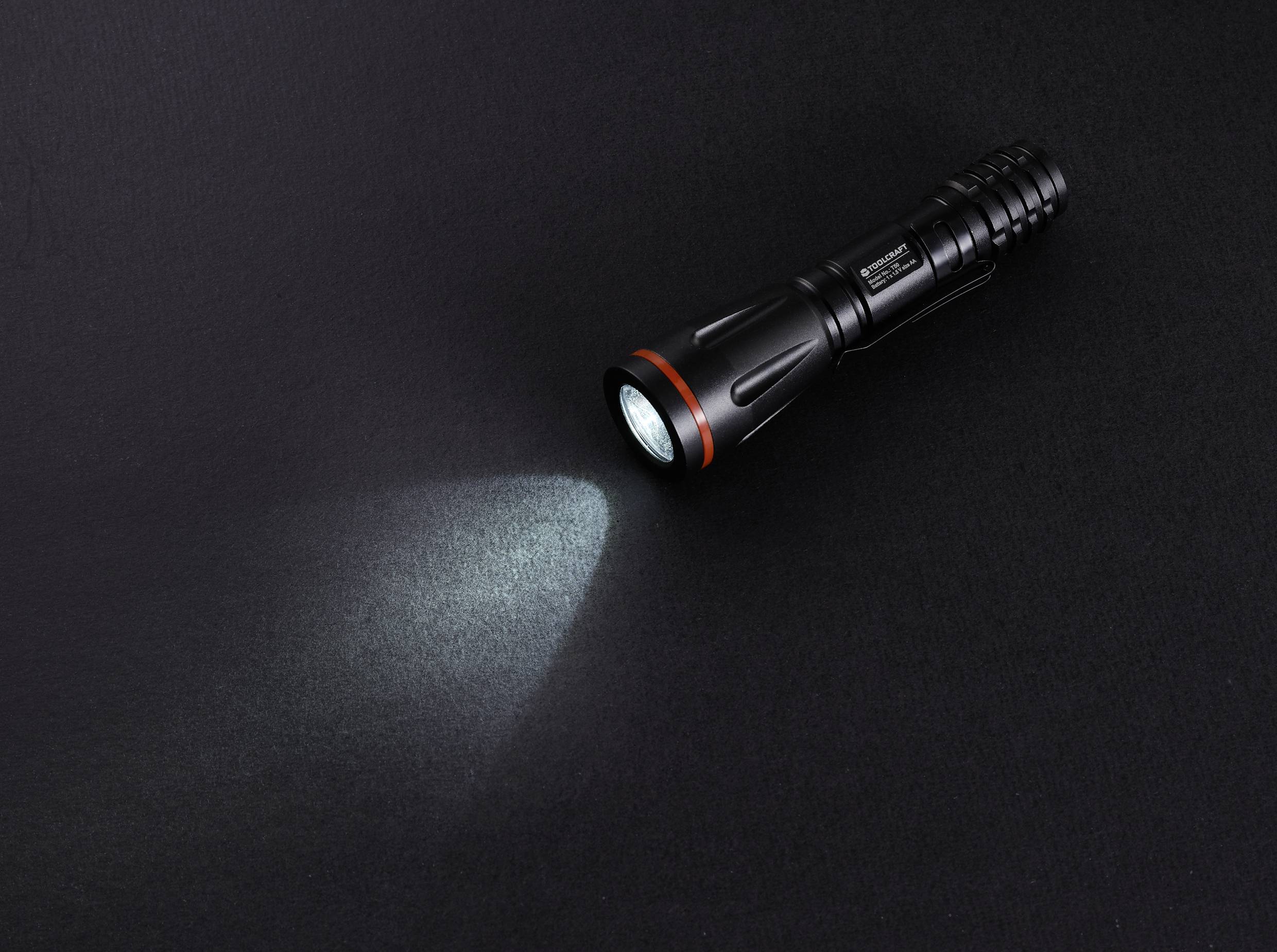 Eine schwarze Taschenlampe leuchtet auf einer dunklen Oberfläche.