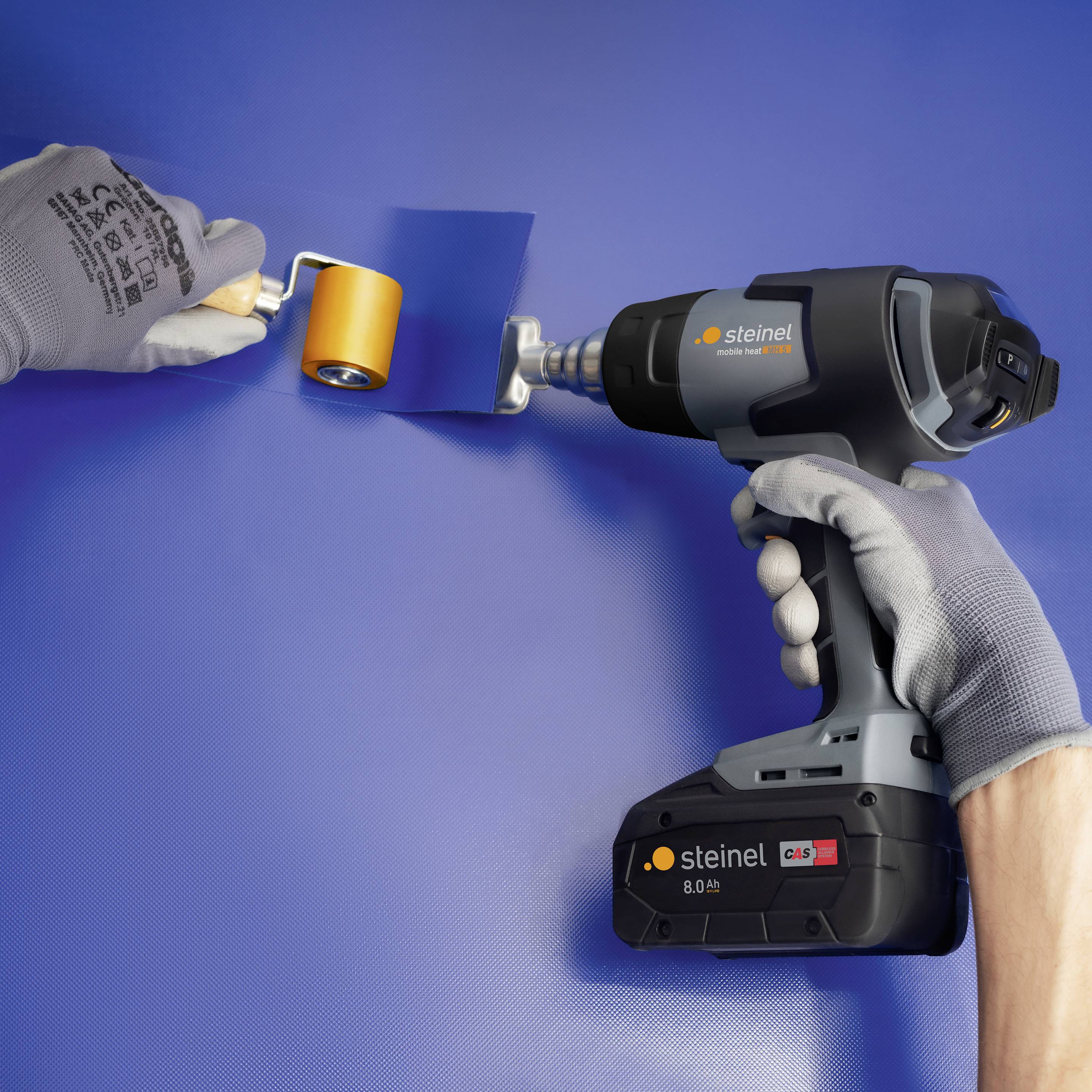 Eine Person hält ein Heißluftgebläse mit der rechten Hand, während sie mit der linken Hand eine Folie oder ein Material mit einer Walze glättet.