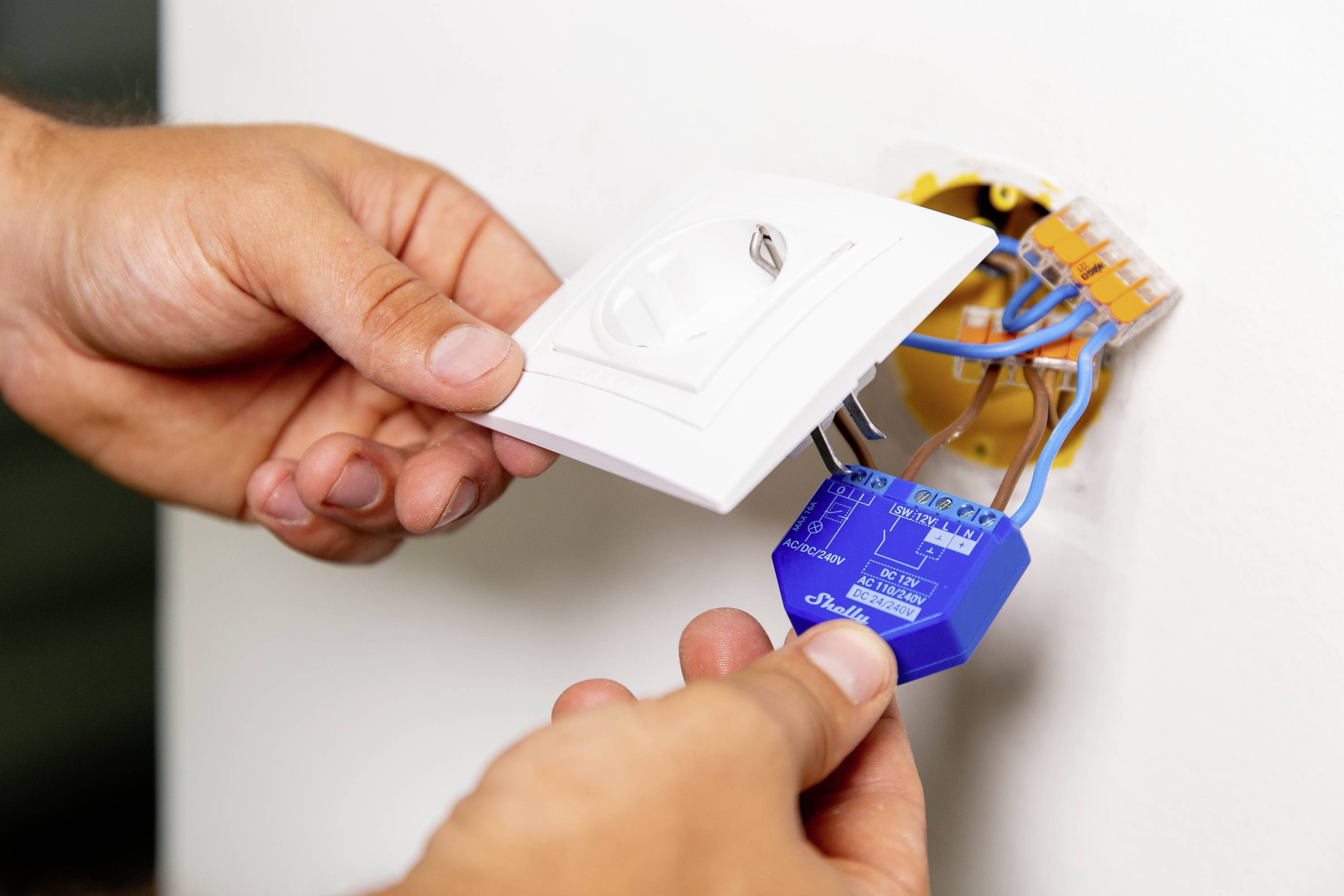 Eine Person installiert einen blauen Dimmer in eine Wandöffnung, wobei sie die Kabel an einem entfernten Lichtschalter anschließt.