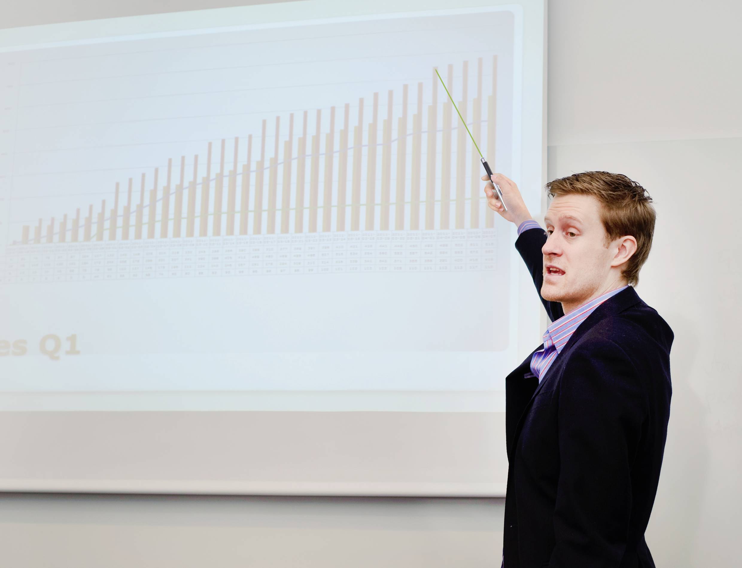 Ein Mann präsentiert ein Balkendiagramm mit ansteigenden Verkaufszahlen für das erste Quartal, zeigt mit einem Zeigestock darauf.