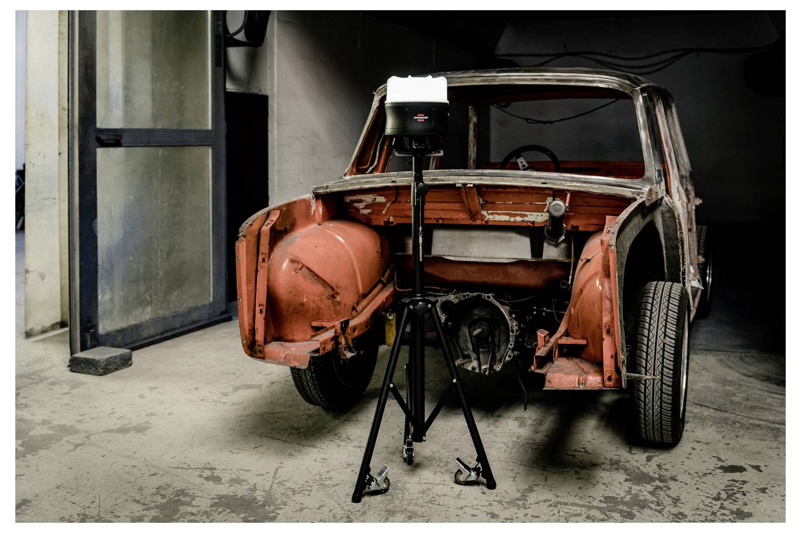 Teilweise restaurierte Karosserie eines Oldtimers in einer Werkstatt, mit einer auf einem Stativ montierten Kameraleuchte, die davor positioniert ist.