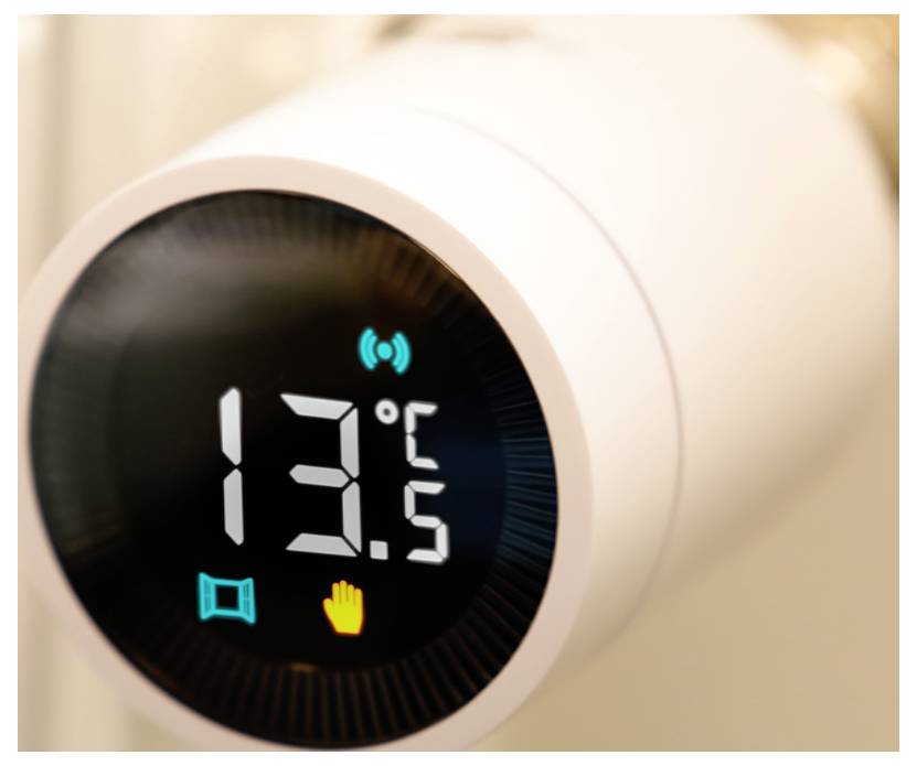 Nahaufnahme eines weißen intelligenten Thermostats, das 13,5°C anzeigt, mit Wi-Fi-, Fenster- und Handsymbolen auf einem schwarzen Bildschirm.